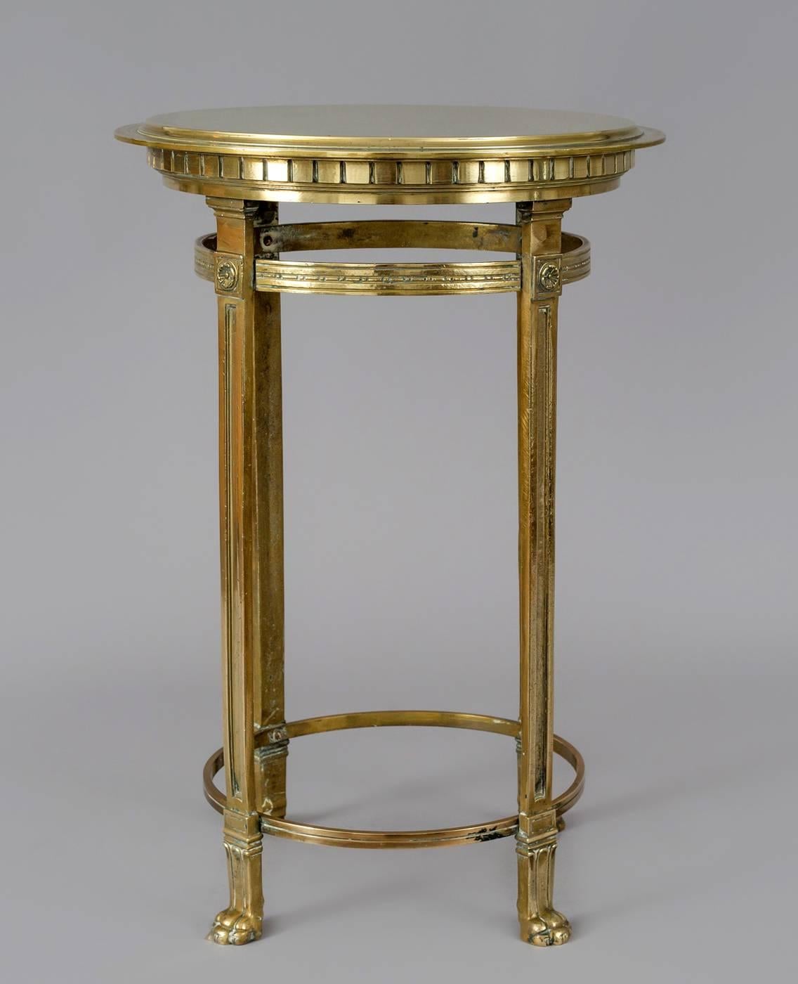 French low round bronze gueridon table with stepped circular top above a dental molded frieze, raised on four straight tapered legs ending in paw feet. The legs are joined by two round stretchers.