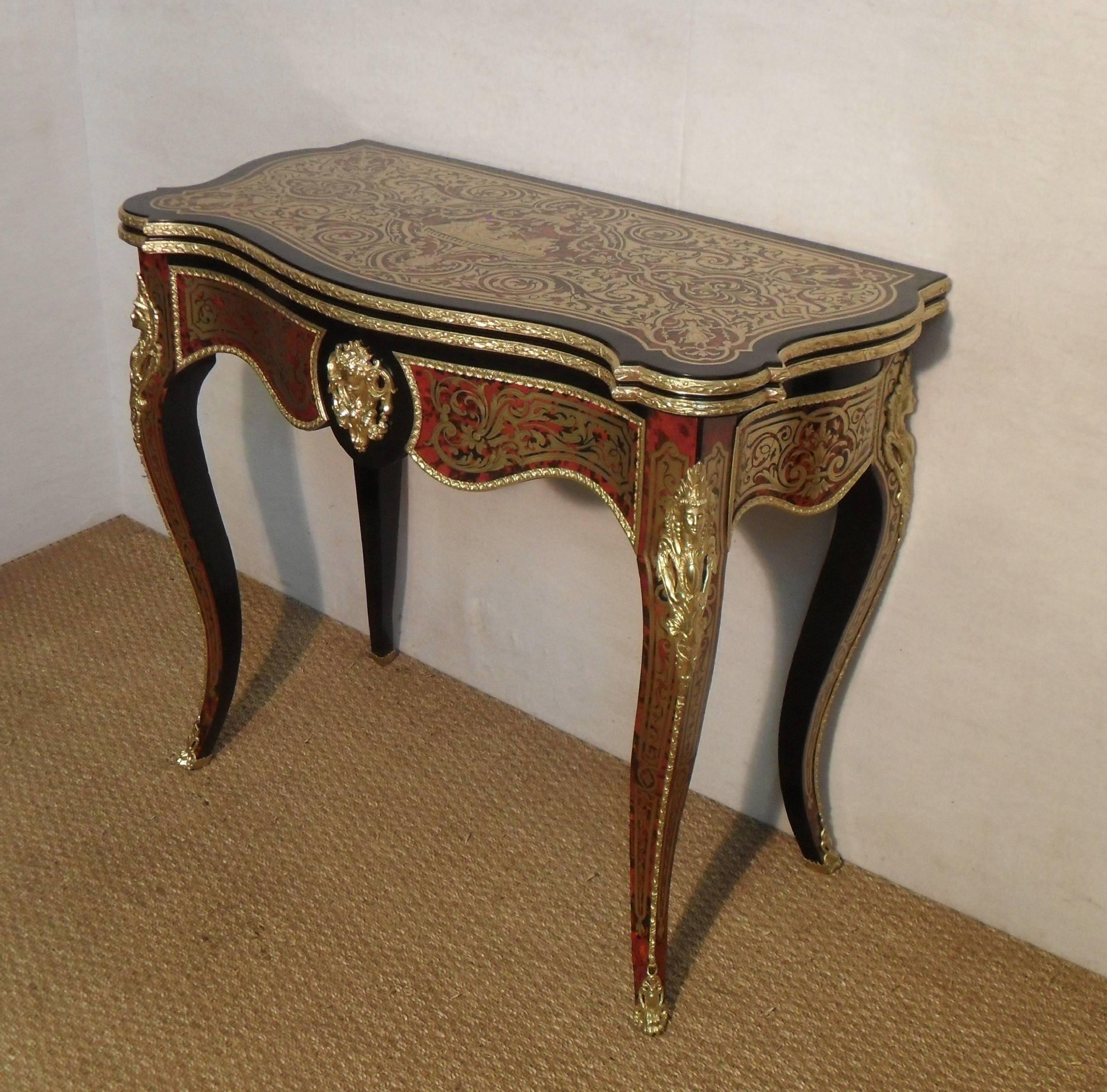 An excellent quality French Napoleon III freestanding serpentine shaped fold over games table inlaid with engraved brass and red tortoise shell with ebonised detail. The top has a central design of cherub on chariot and horses with a decorative