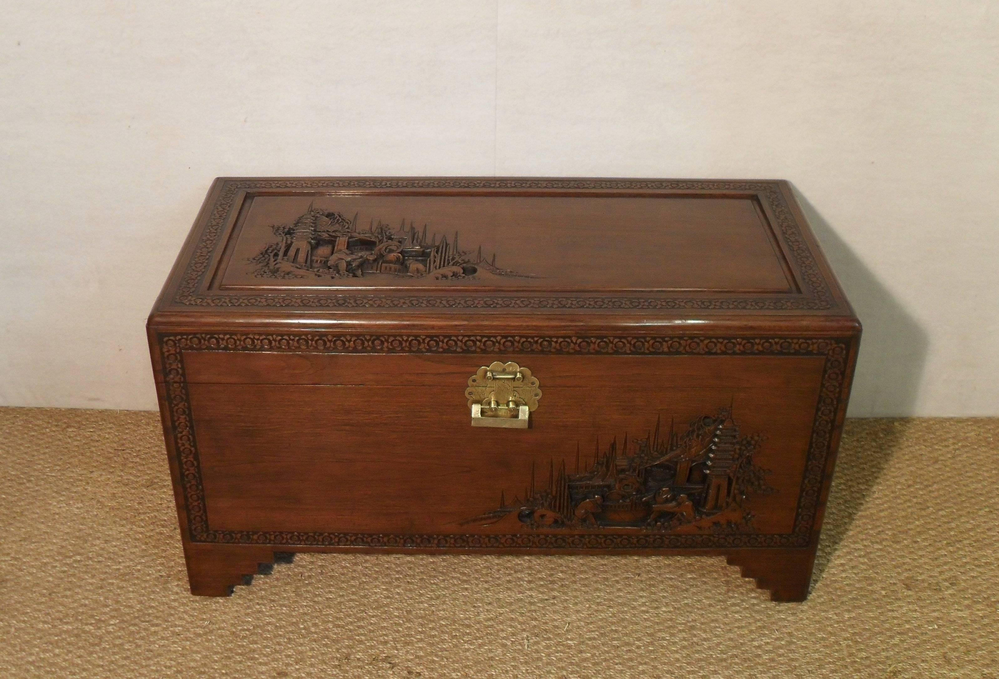 A good quality oriental camphor wood chest on stepped bracket feet with detailed landscape carvings and carved floral border to the front and top.

The chest retains its original decorative engraved brass back plate and latch and comes with a
