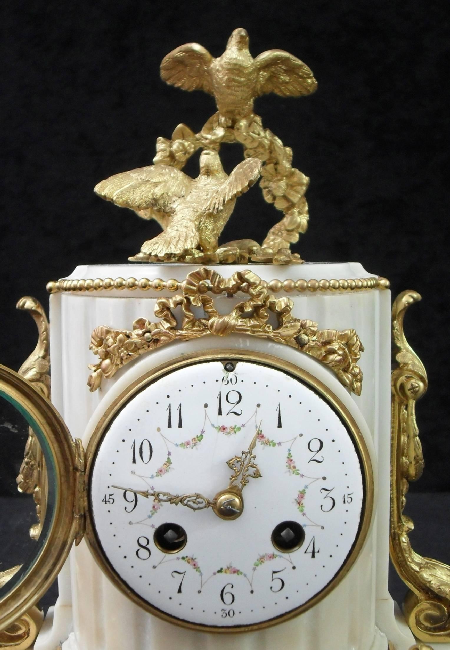 A very good quality white marble mantel clock with decorative ribbon and floral bronze gilt ormolu mounts surmounted by two doves. The clock has a white enamel dial with painted detail and an eight day French movement which strikes the hours and
