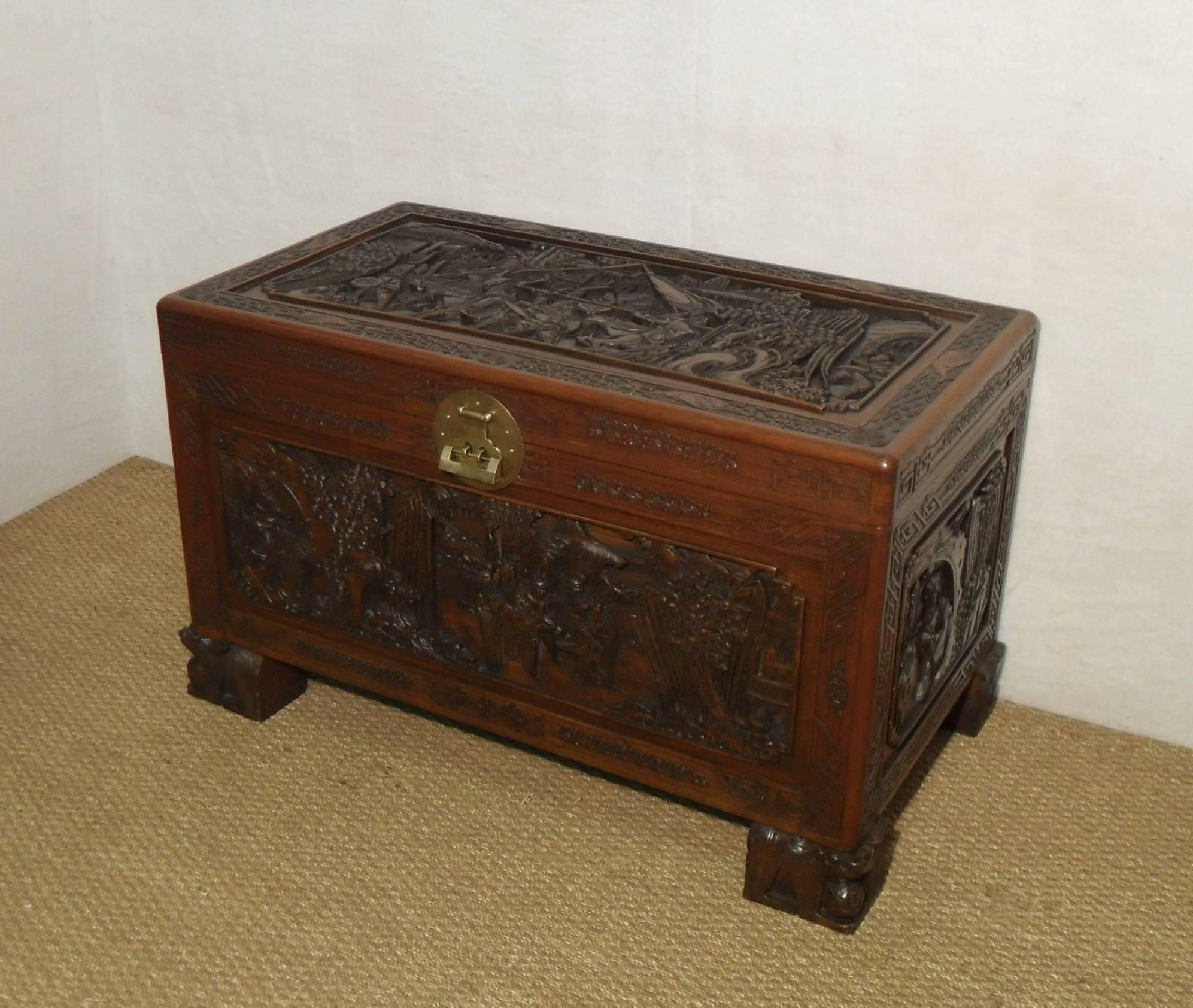An extremely good quality and ornately carved freestanding oriental camphor wood chest with deeply carved scenes of warriors, horses, trees and pagodas surrounded with a floral, cloud and crane border. The chest retains its original engraved brass