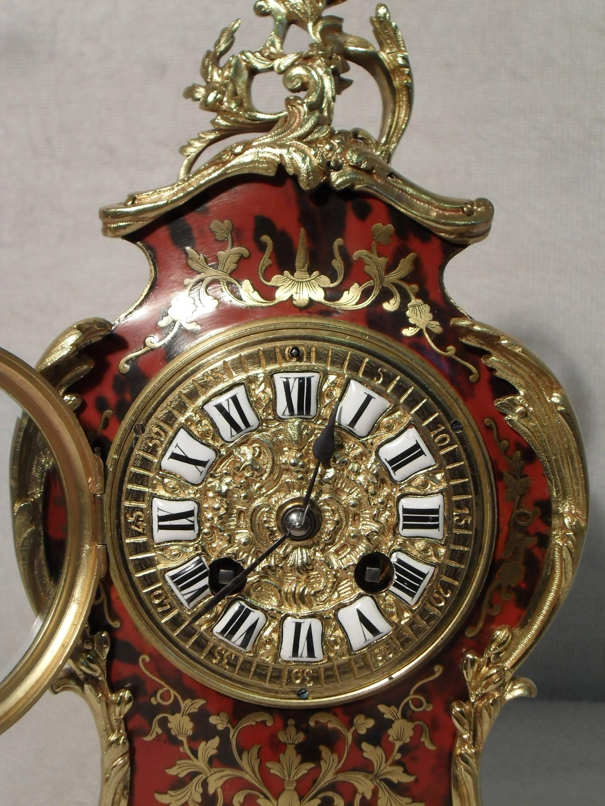 ?A very good quality French Louis XV style serpentine shaped boulle red tortoise shell and engraved brass mantel clock with scroll leaf ormolu mounts. The clock has a decorative brass dial with white enamel numerals and a French eight day movement