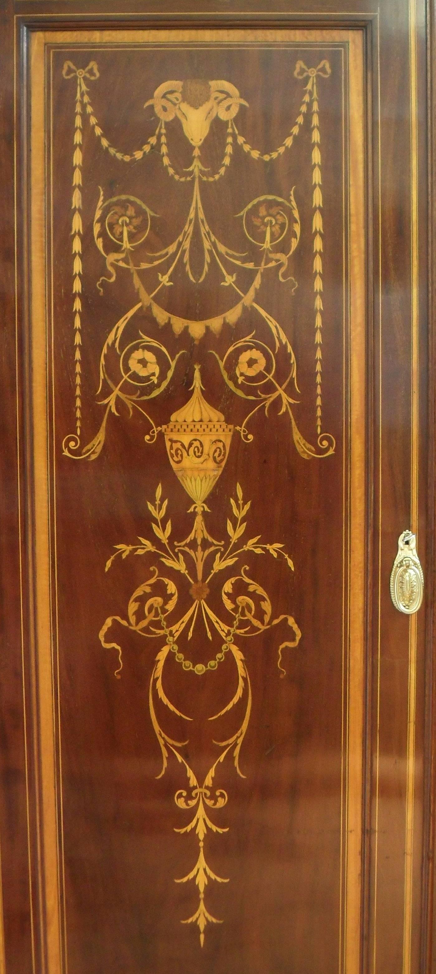 A magnificent quality Edwardian mahogany Sheraton revival wardrobe with fabulous cornice. The cornice has Greek key mouldings and swan neck pediment with a central rose and pierced fret work. The door panels are beautifully inlaid with a ram's head,