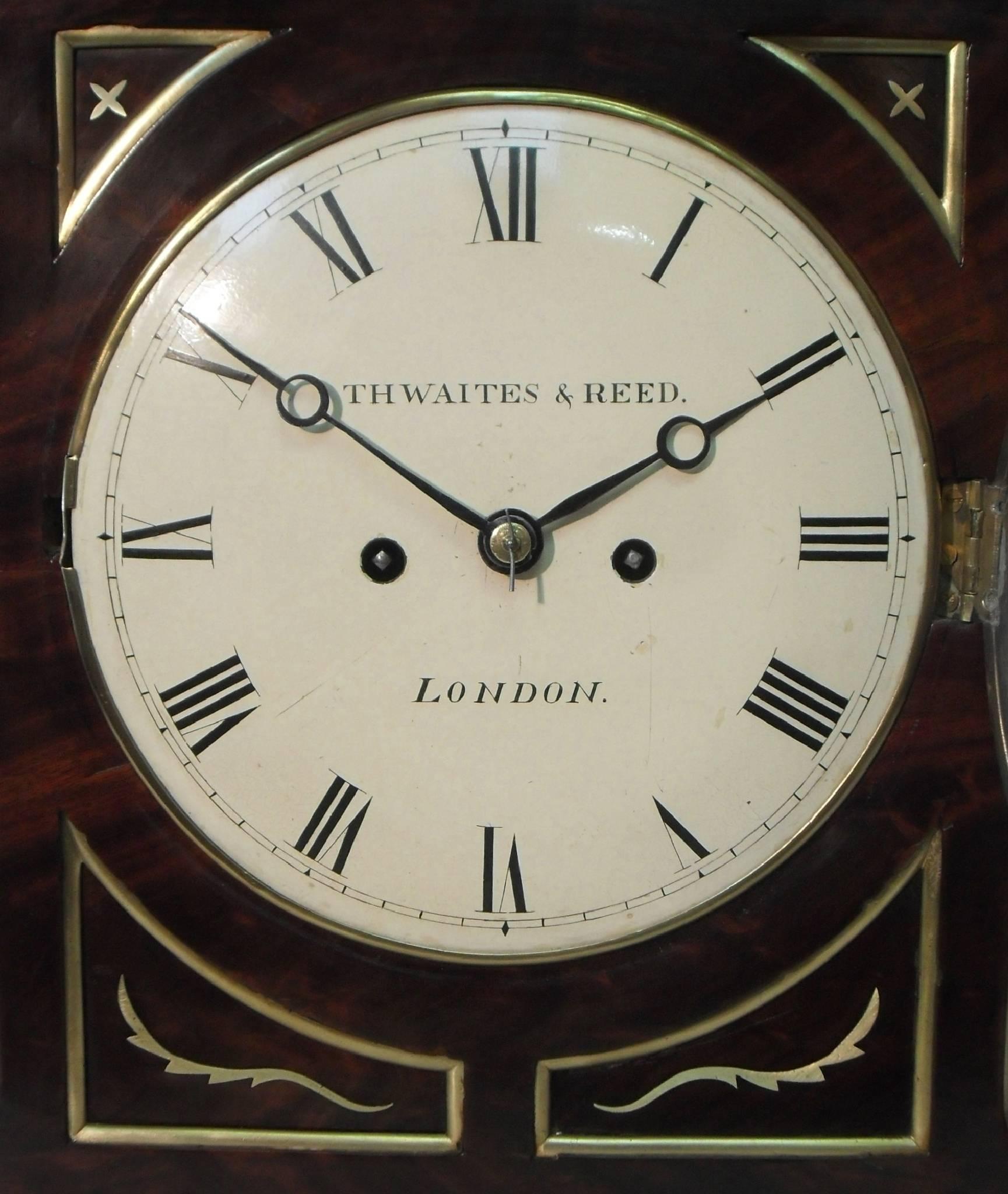 An extremely good quality English figured mahogany chamfer top bracket or table clock with ebony moulding, decorative brass inlay, inset corner panels and brass moulded edges to the front stood on brass ball feet finished with a pineapple finial to