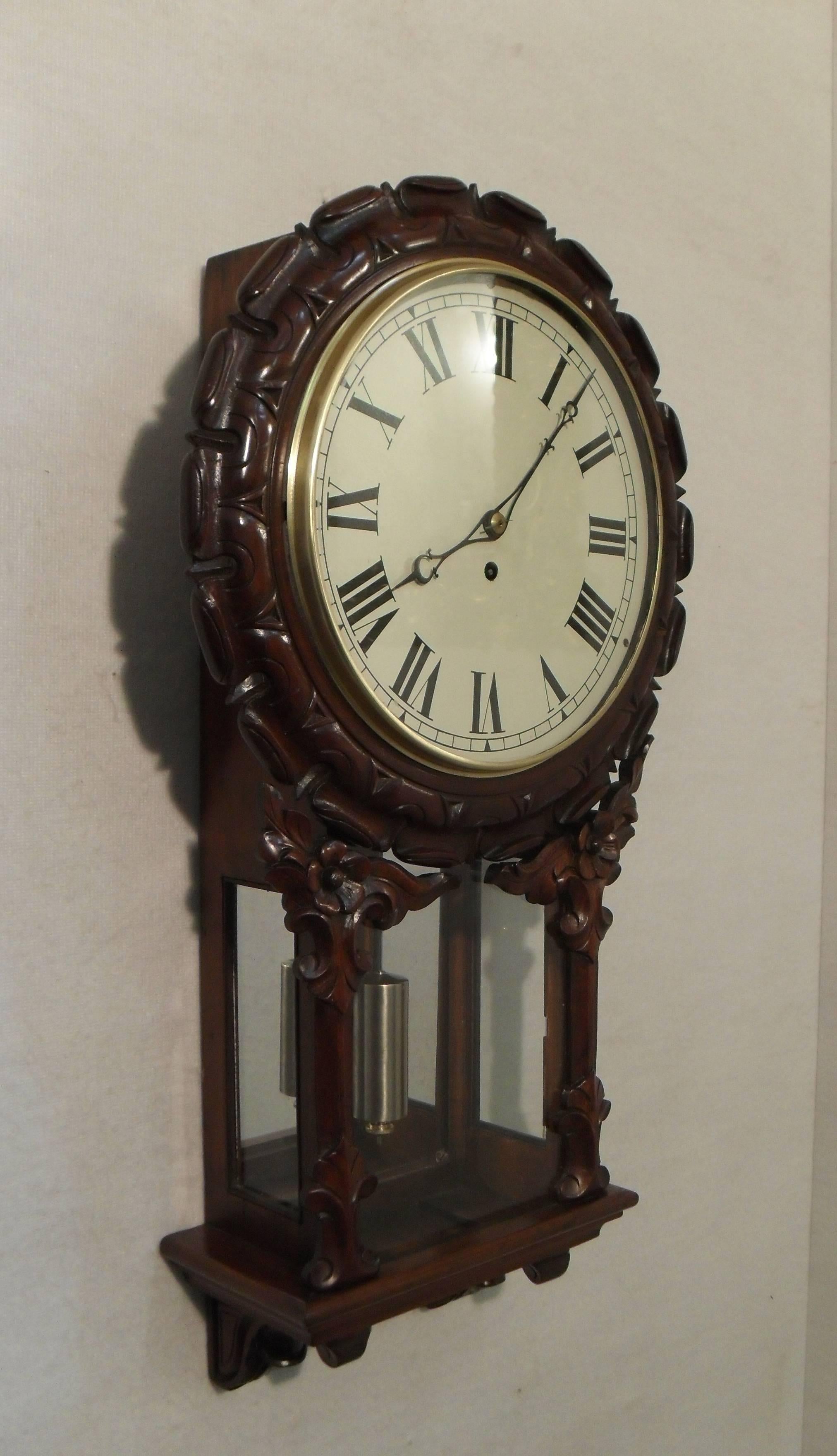 A good quality carved mahogany drop dial wall clock with mirror back to the pendulum viewing window. The clock has a painted twelve inch dial with an eight day, single fuse timepiece movement and anchor escapement.

The movement has been cleaned
