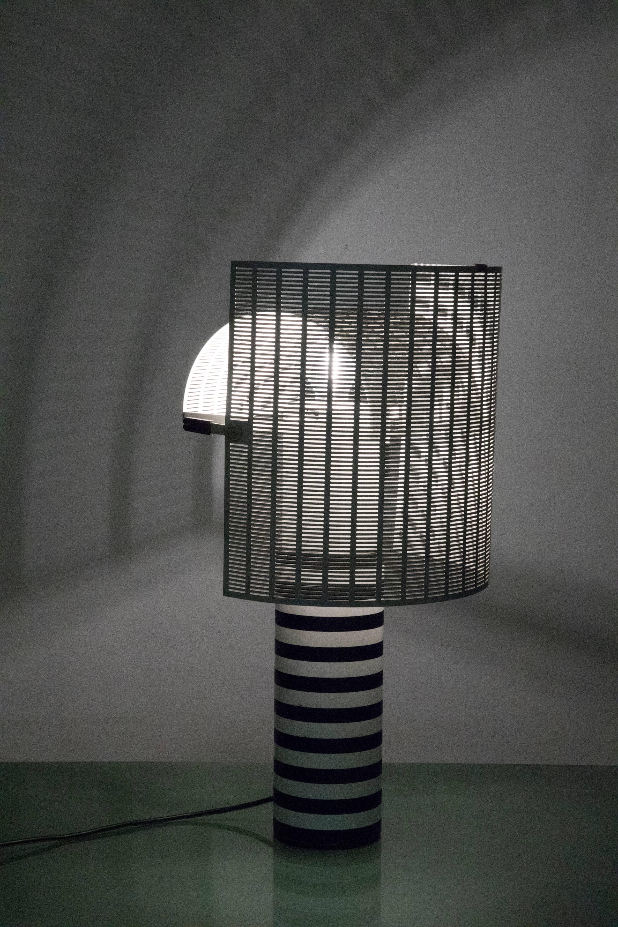 Italian table lamp designed by Mario Botta in 1986 for Artemide and no longer in production.
The black base is made of cast iron, the powder coated shaft is black and white striped. Two curved perforated diffusers can be pivoted to create endless