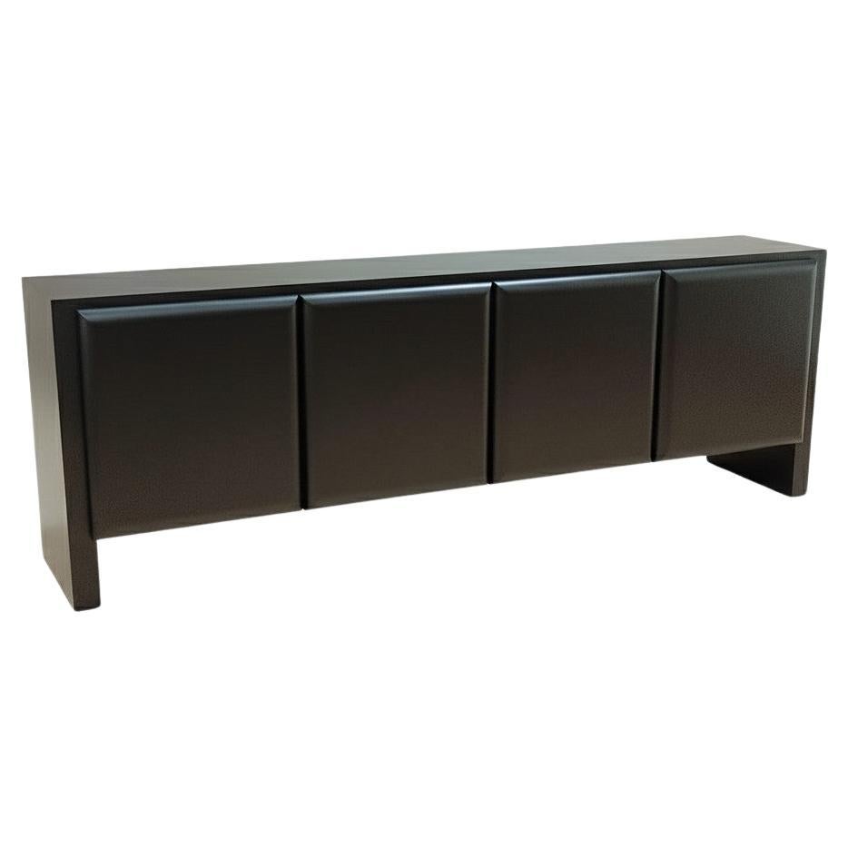 A long, modern sideboard in a dark stained Oak, almost black color with a very dark brown espresso shade. The piece of furniture has a rectilinear, minimalist design. The top surface is flat and smooth with visible wood grain. The front is divided