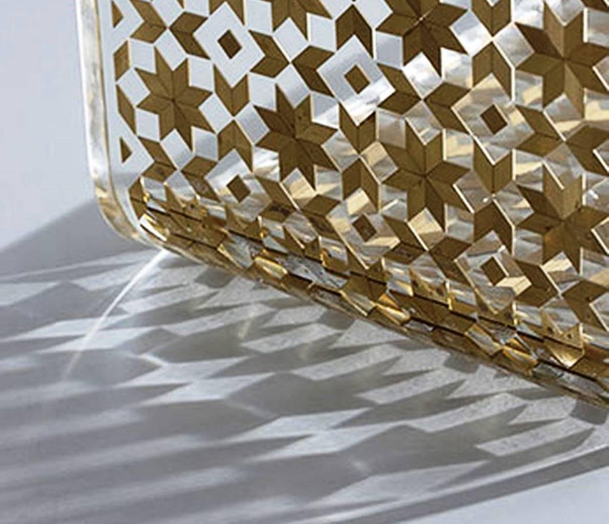 The C Resin side table by Nada Debs is composed of transparent resin with hand inlay of mother-of-pearl, brushed silver metal or brushed brass and copper metal; reflecting the beauty of Arabesque geometric designs. 

This practical table slides