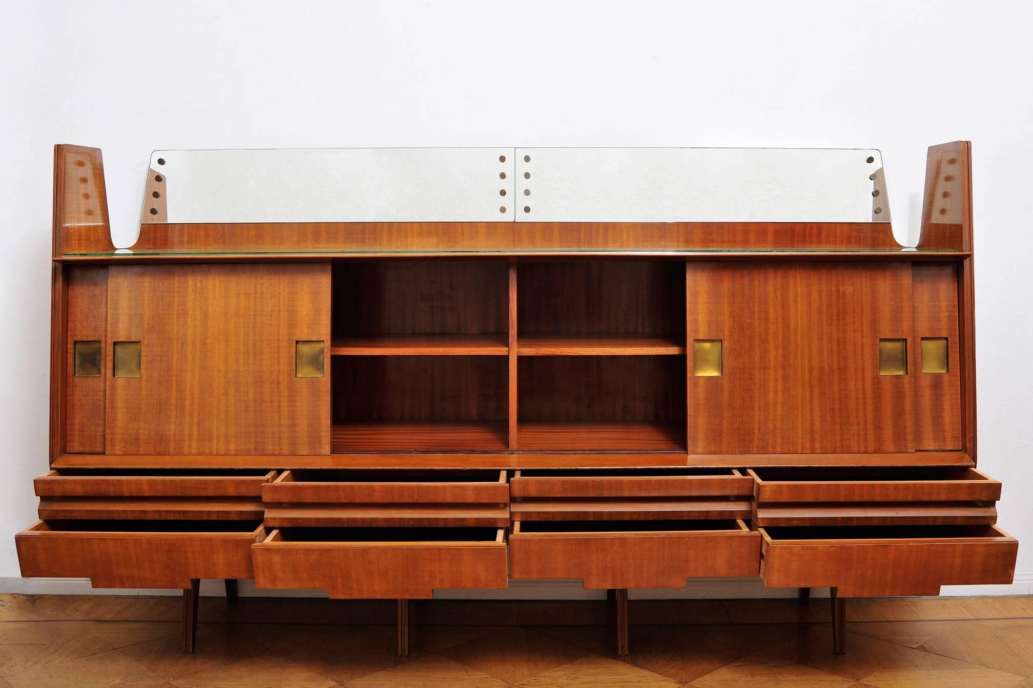 20th century Italian sideboard from the 1960s made of teak with brass handles, a glass top and mirror back border. The sideboard has eight drawers and four sliding doors behind each of which is a removable shelf.