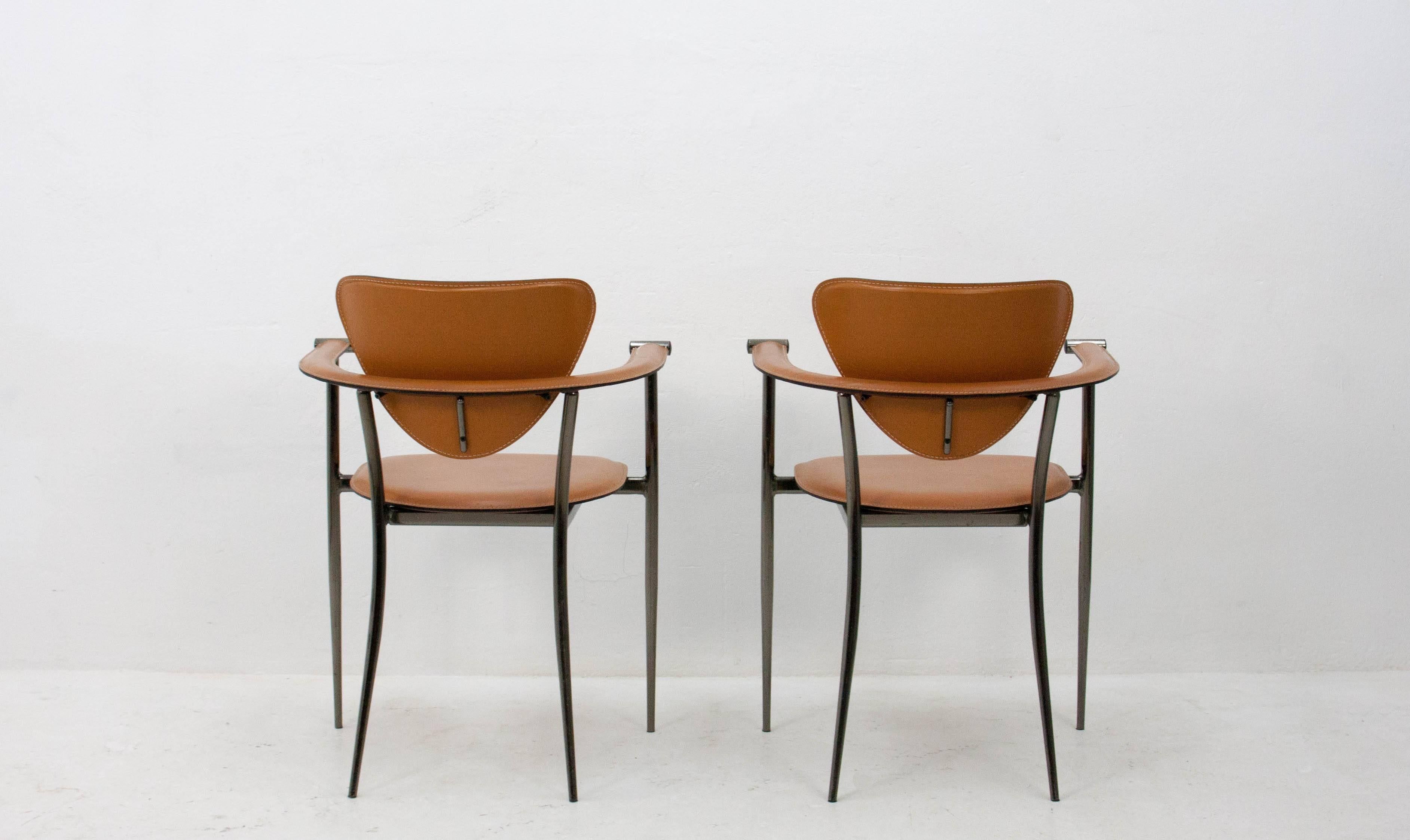 A pair of Italian Arrben chairs upholstered in a hand-stitched cognac leather on a dark chrome frame with semi-circular armrests.