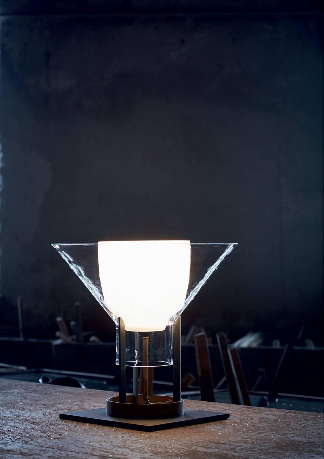 Lampe de table en verre de Murano transparent soufflé à la bouche, fer peint anthracite et laiton naturel, conçue en 1984 par Carlo Moretti et Paolo Martinuzzi. 

ampoule à incandescence de 60 watts, douille ecolamp de 42 watts E27.


Carlo