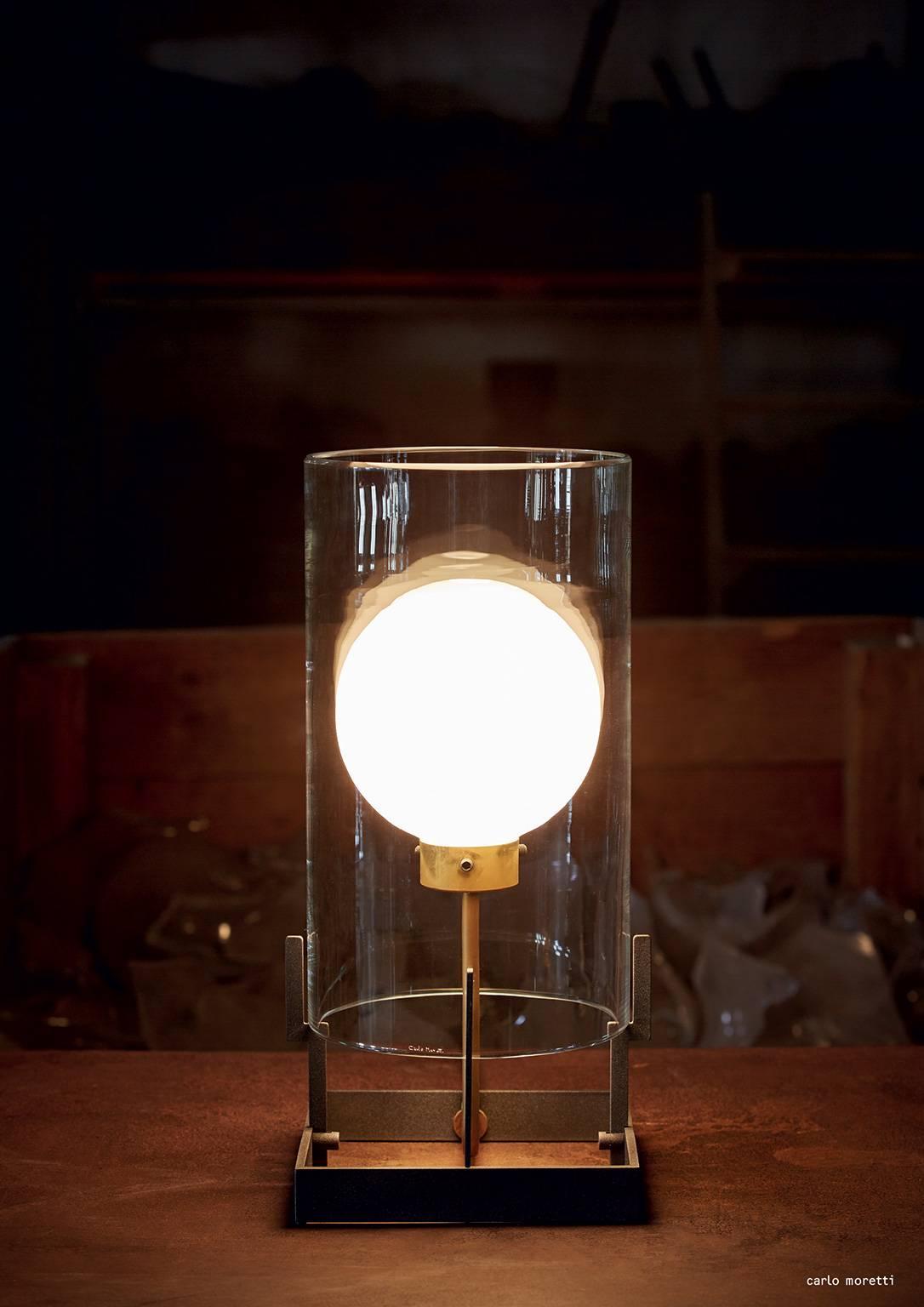 Tischleuchte aus klarem mundgeblasenem Muranoglas, anthrazitfarben lackiertem Eisen und natürlichem Messing, entworfen 1984 von Carlo Moretti und Paolo Martinuzzi. 

60-Watt-Glühlampe, 42-Watt-Ecolamp-Fassung E14.


Carlo Moretti: Eine