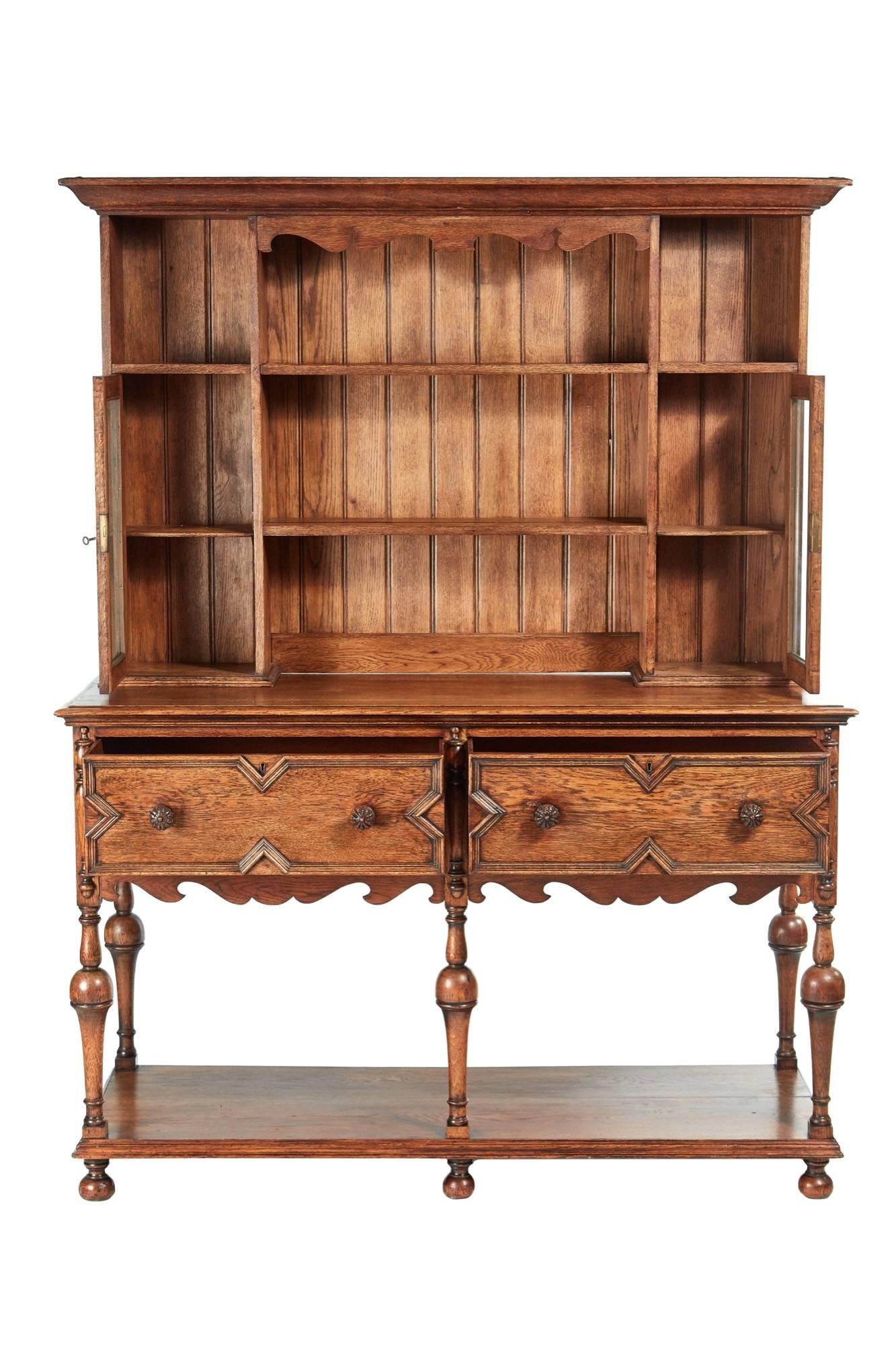 Antique oak welsh dresser, top section with a shaped cornice, solid oak back, plate rack with two glazed doors, the base with two large drawers original carved oak knobs, shaped frieze, five turned shaped supports, shelf base standing on original
