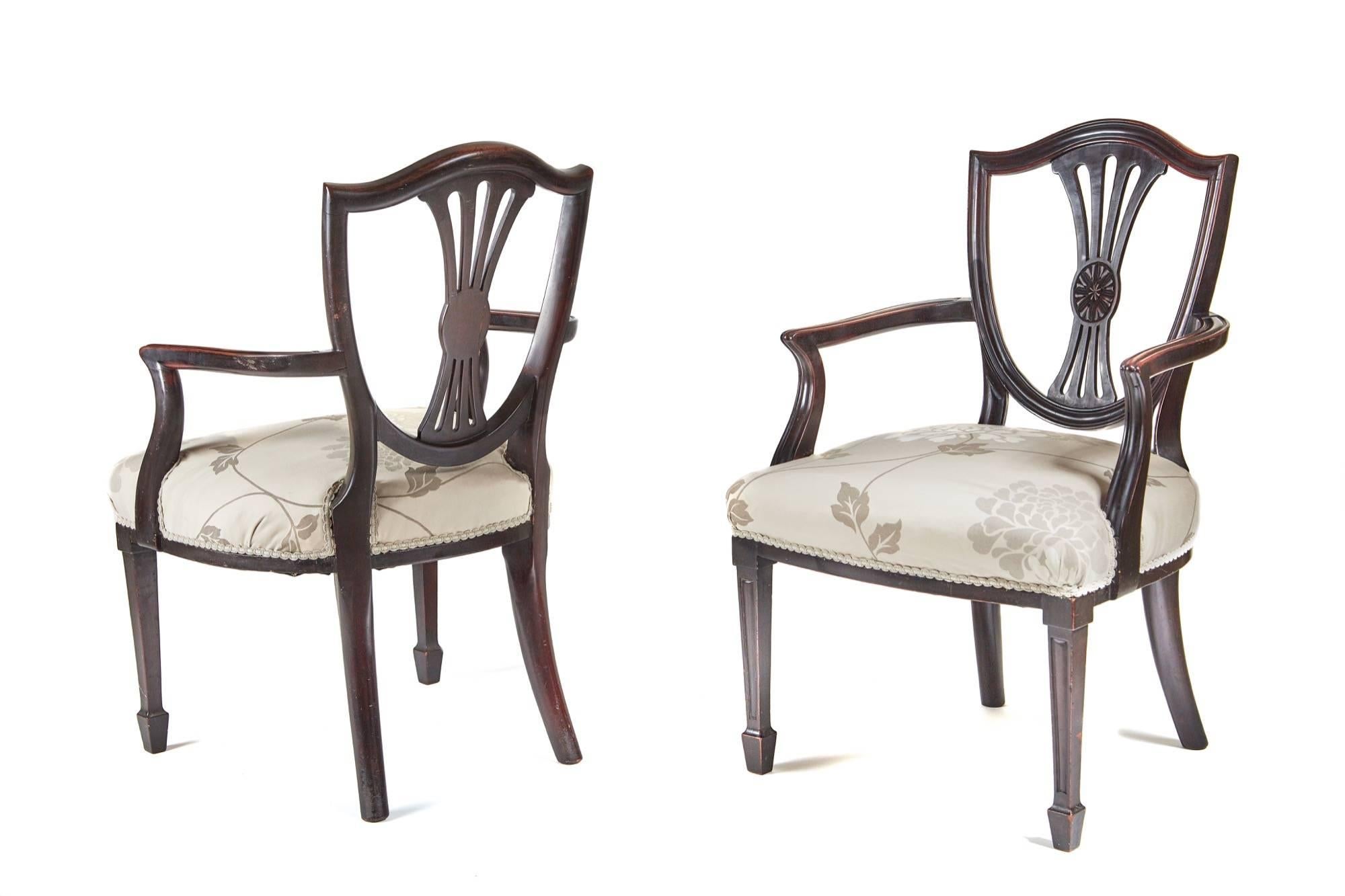 A pair of mahogany Hepplewhite style elbow chairs, with a shield shaped back and a pierced reeded central splat, nice reeded shaped arms, the overstuffed wide seats have been recovered in a very attractive fabric, the front legs are square tapering