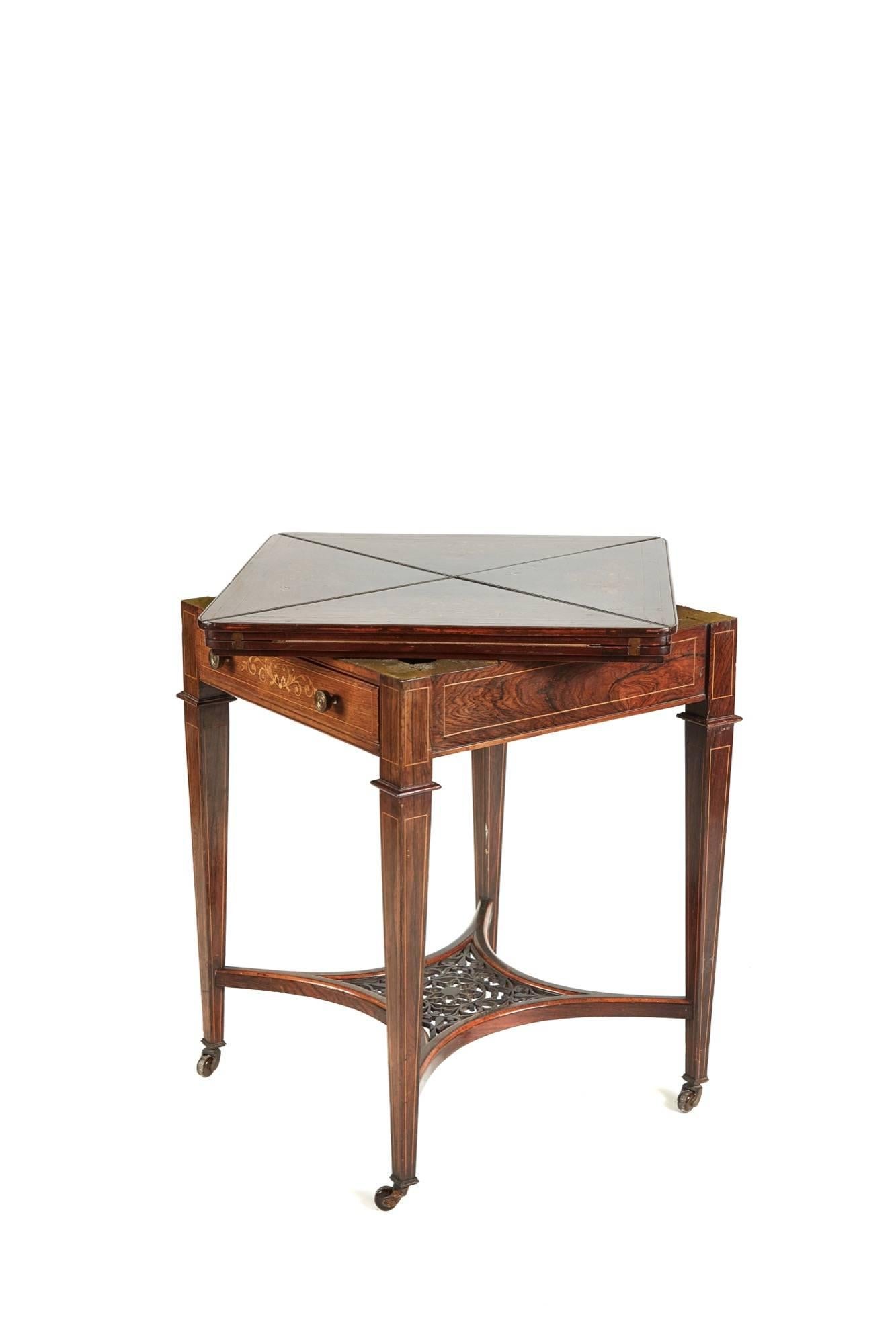 A rosewood and marquetry inlaid envelope card table, the fold-over top opening to reveal baize lined playing surface above a frieze drawer, the platform under tier with fret carved centre section, inlaid square tapering legs with original