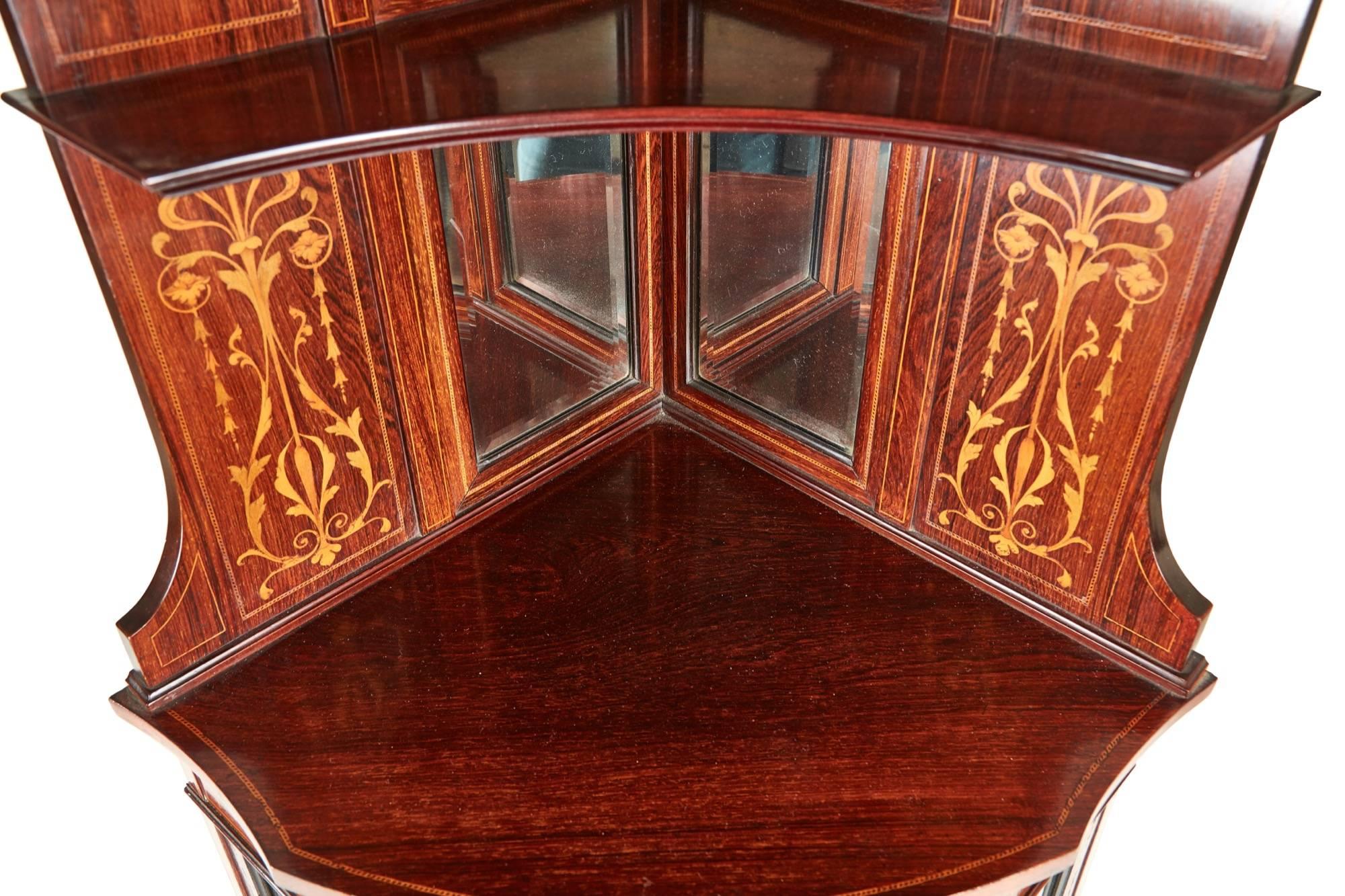 Outstanding rosewood inlaid corner cabinet, the top with six bevel edged mirrors, marquetry inlaid satinwood panels, the bowfront base with a glazed centre door, marquetry inlaid satinwood frieze, supported by tapered legs with spade feet united by
