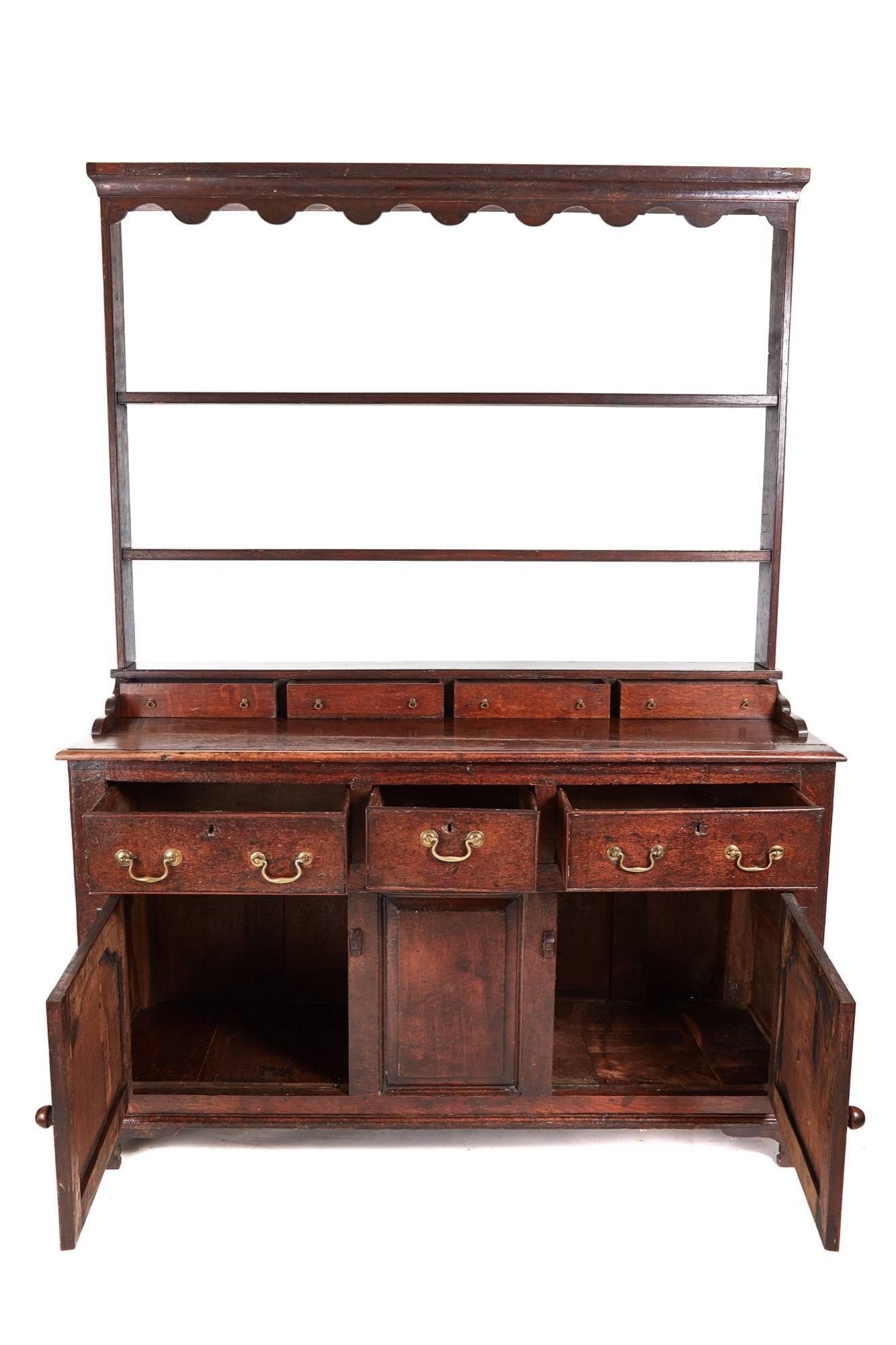 Early 18th century oak welsh dresser, with a swept ogee cornice, plate rack, and four drawers with original brass handles, the base with two cupboard doors, each with raised shaped panels, and a centre raised panel, three drawers with original brass