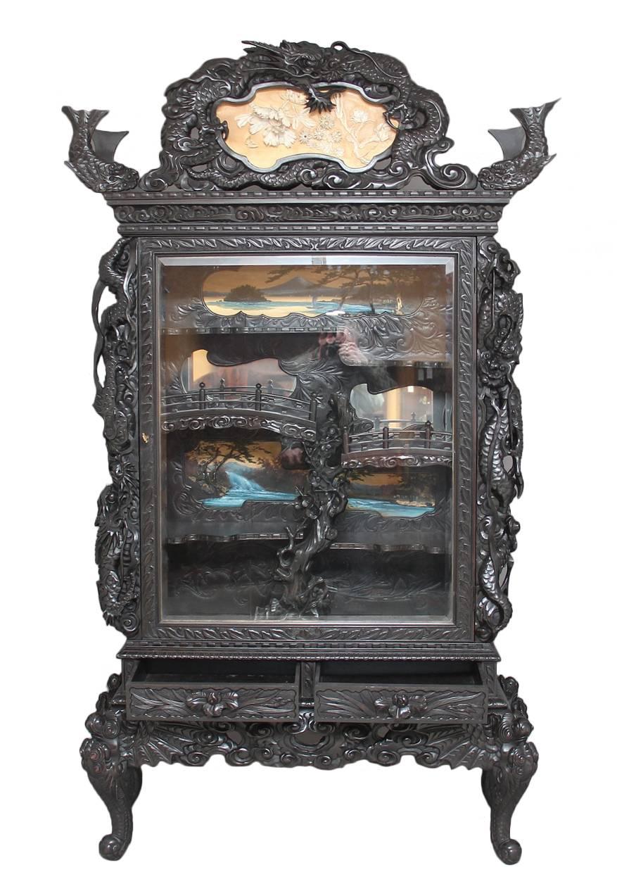 Large unusual carved Japanese display cabinet, the pediment carved with fish and dragons with a set back panel with flowers and a butterfly carved in bone, below the pediment is a single glazed door which is also richly carved, the main cabinet with