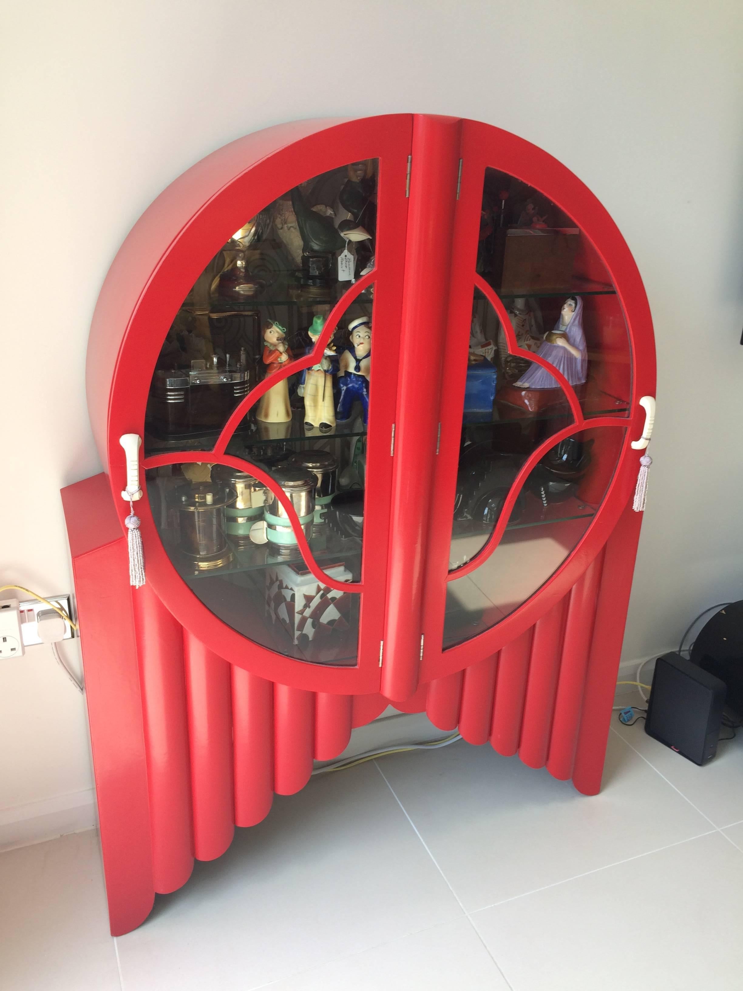 Walnut rocket display cabinet with cream phenolic handles in a wild red lacquer. Four internal glass shelves. The backboard is covered in an Art Deco design covering. It measures 53.5 inches tall by 40 wide by 13.5 deep (136cm x 102 x 34). Very good