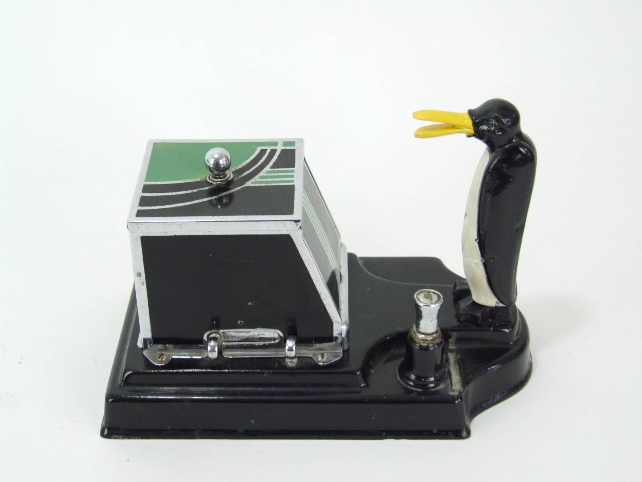 A strike-lite penguin cigarette box and lighter with black and green enamel box, chrome knob and black metal base, circa 1934. The Penguin is rarer than the monkey version. Squeeze the levers to the front and the penguin will pick up a cigarette