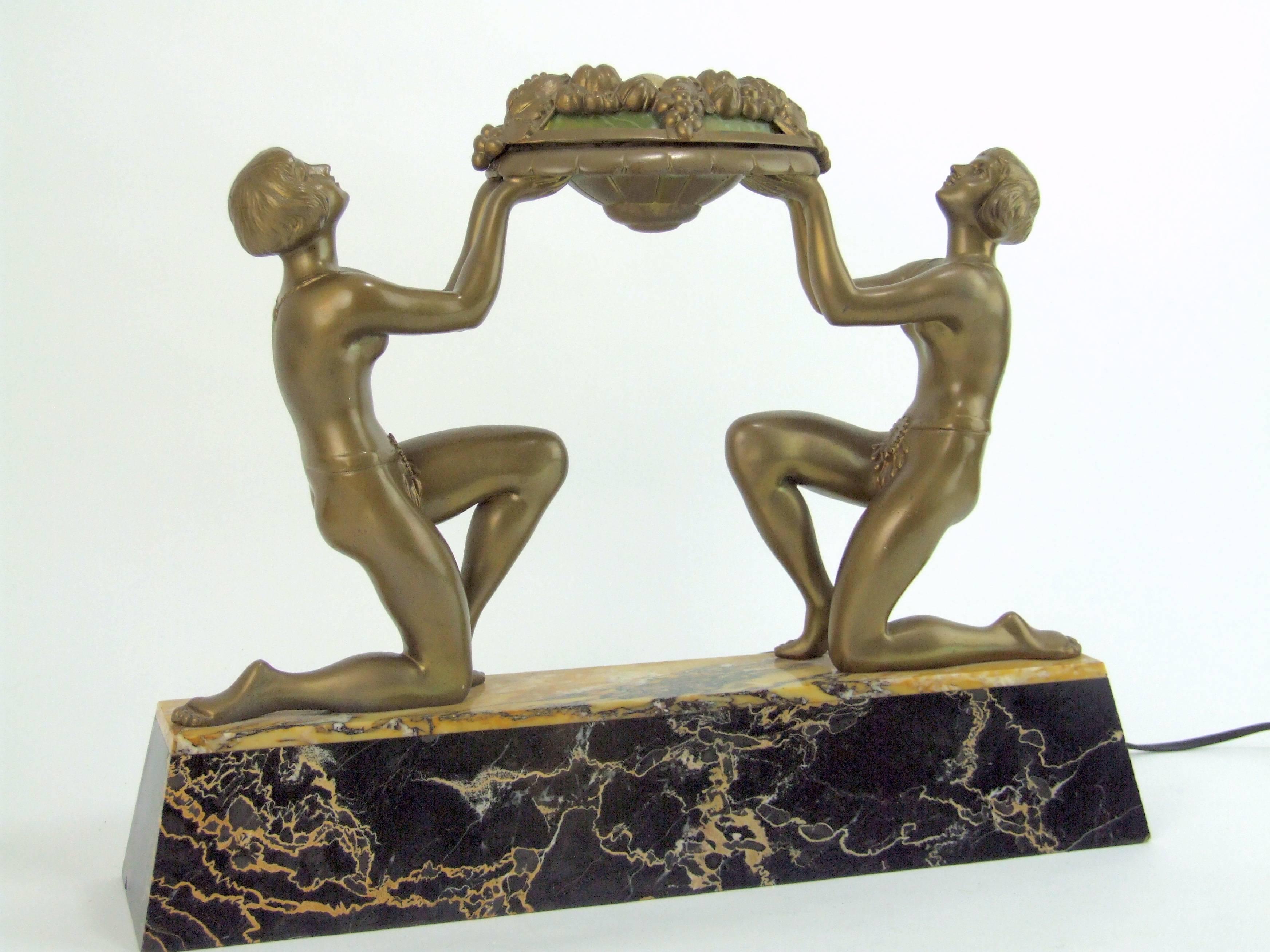 French spelter Art Deco double lady lamp. A signed Limousin. The top section is the lamp cover and has phenolic green panel inserts. Mounted on a portorro and sienna marble base, it measures 16.5 inches wide by 3.75 inches deep by 12.5 inches high