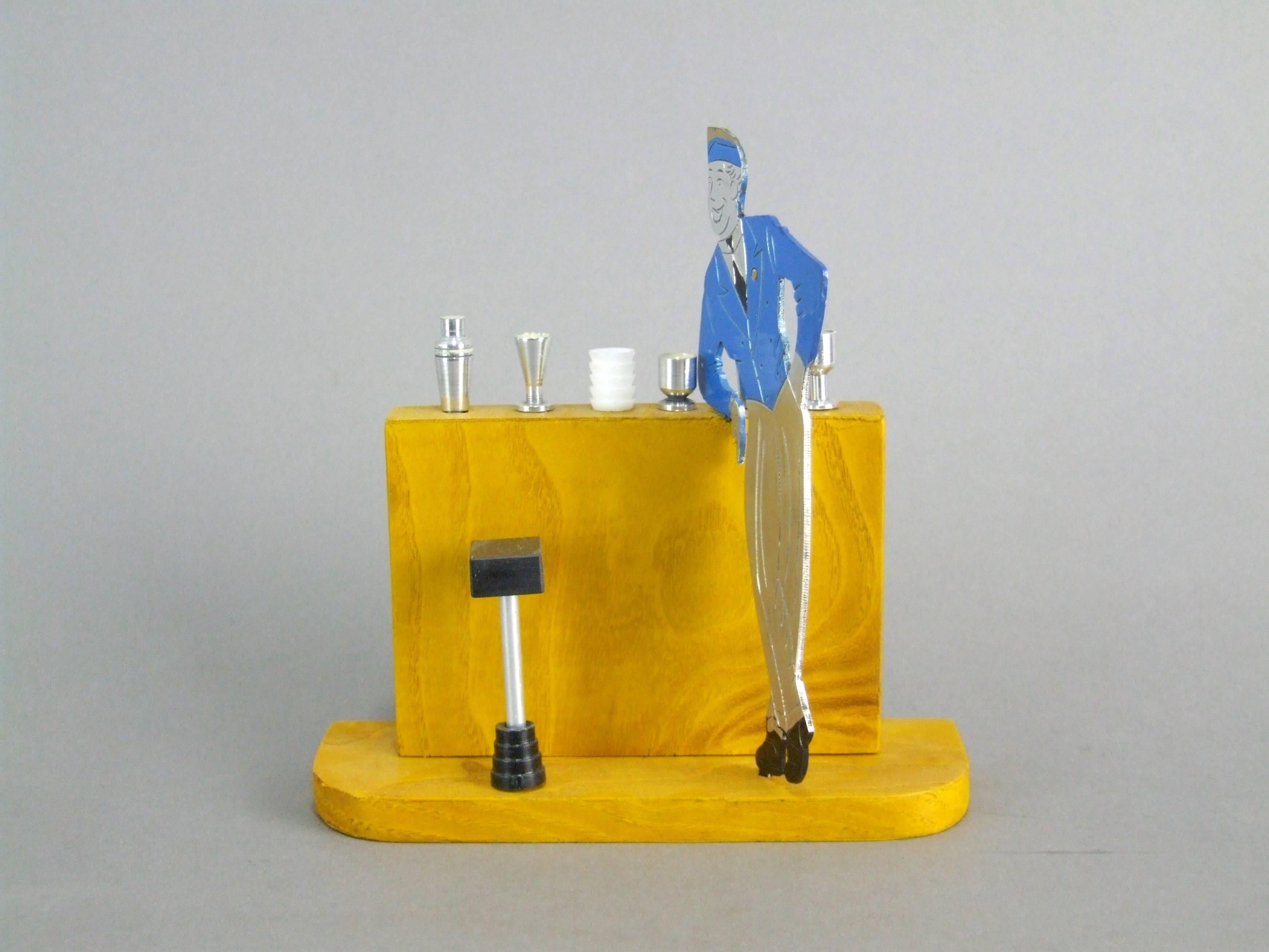 Two dimensional airman standing at a bar. The items on the bar are pullout cocktail sticks. The base is wooden and measures 5.5 inches long by 2 inches deep and the total height is 5.75 inches (14cm x 5cm x 14.5cm). The set is French and an unsigned
