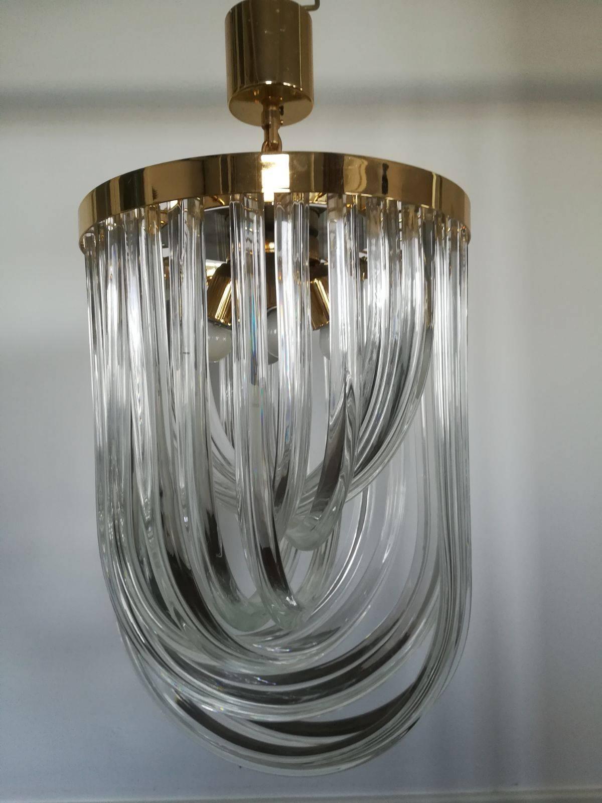This large Mid-Century Modern chandelier by Paolo Venini features 12 individually handmade and curved Murano Crystal clear glass prisms on a brass frame.

The curved glass prisms reflects the light in a beautiful way, the shape seems to change as