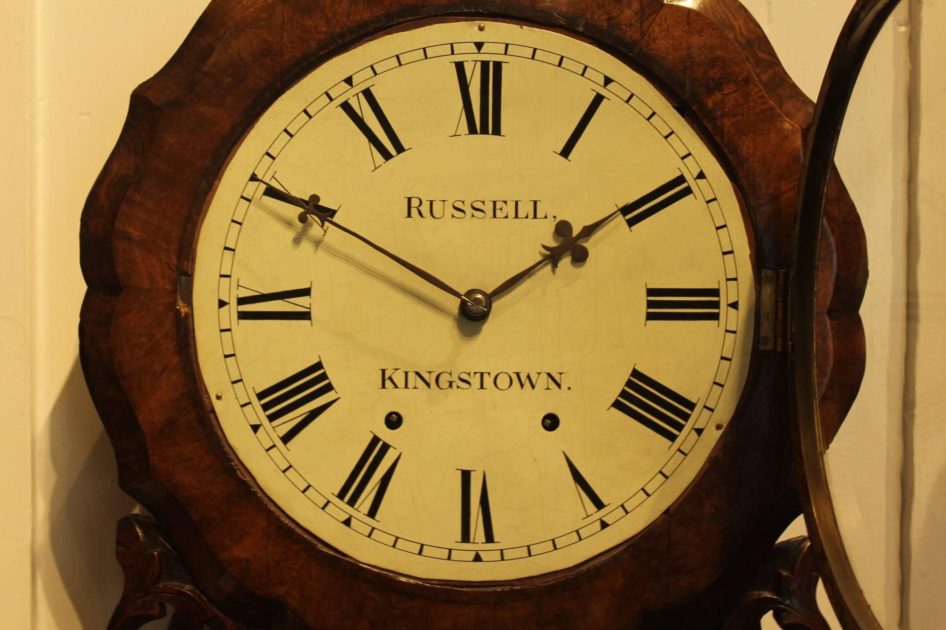 This Anglo-American wall clock from circa 1870 is housed in a particularly beautiful walnut case which is embellished with decorative carvings. It has a wonderful scalloped head around the clock surrounds. This is intricate work and lost as