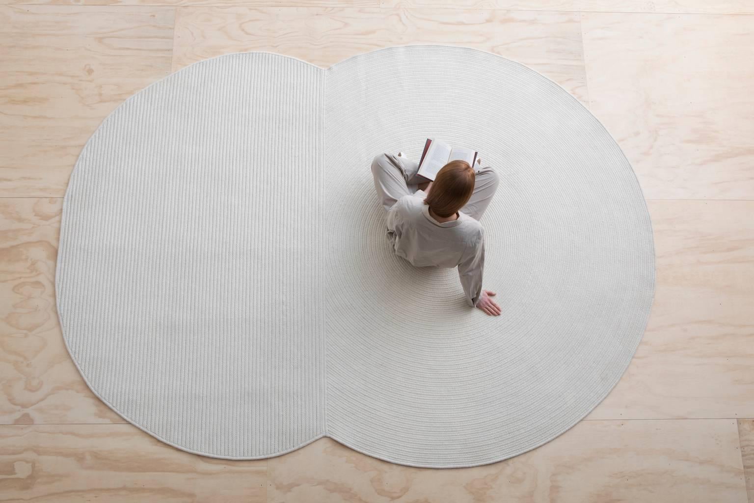 A braided wool rug composed of a simple circle and oval shape bound together. Each shape explores a subtle contrast in braiding technique with the circle made of a flat braid coil and the oval made of cable lock braided rows with a contrasting zig