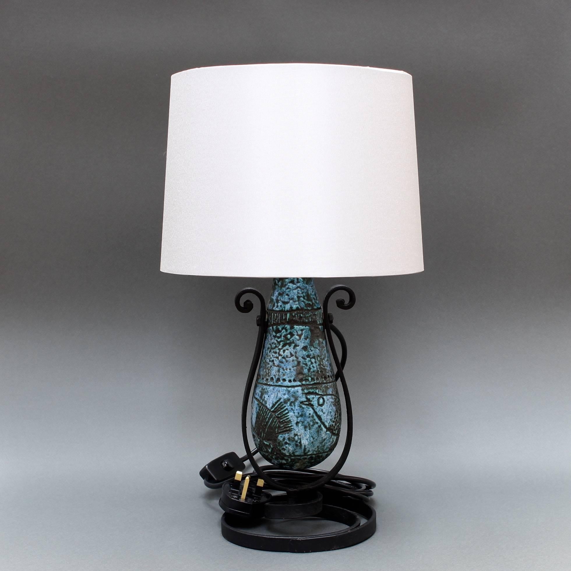 Blue ceramic pivoting table lamp (circa 1950s) by Jacques Blin (1920-1995). This lamp has Blin's signature blue cloudy glaze featuring etchings of fanciful images of birds walking the grounds. The lamp pivots on the wrought-iron base. It is in