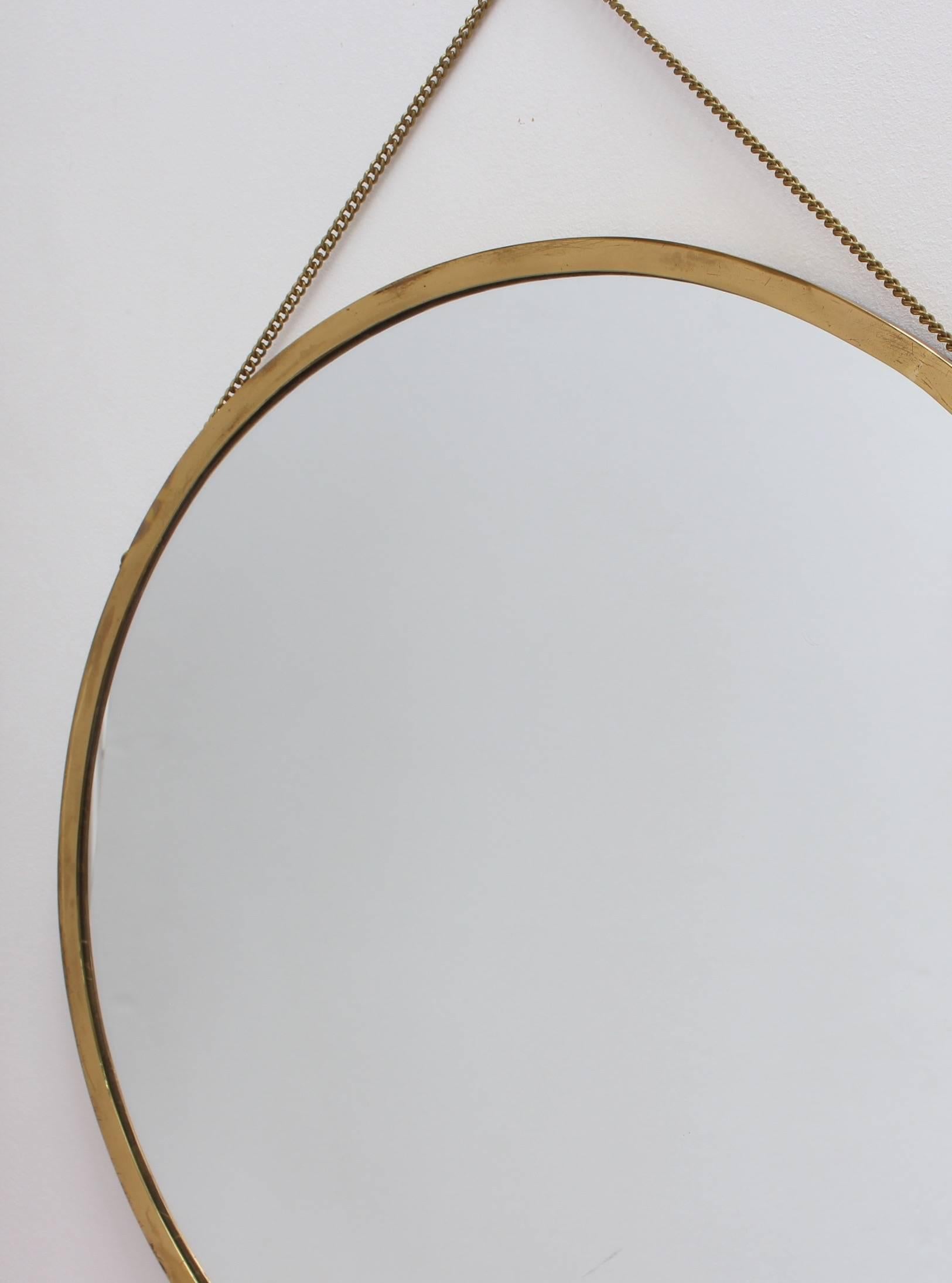 Midcentury Italian wall mirror with brass frame, circa 1950s. The mirror is perfectly circular with an attached brass hanging chain. The effect is so elegant and very distinctive in a modern Gio Ponti style. This mirror is in good vintage condition.