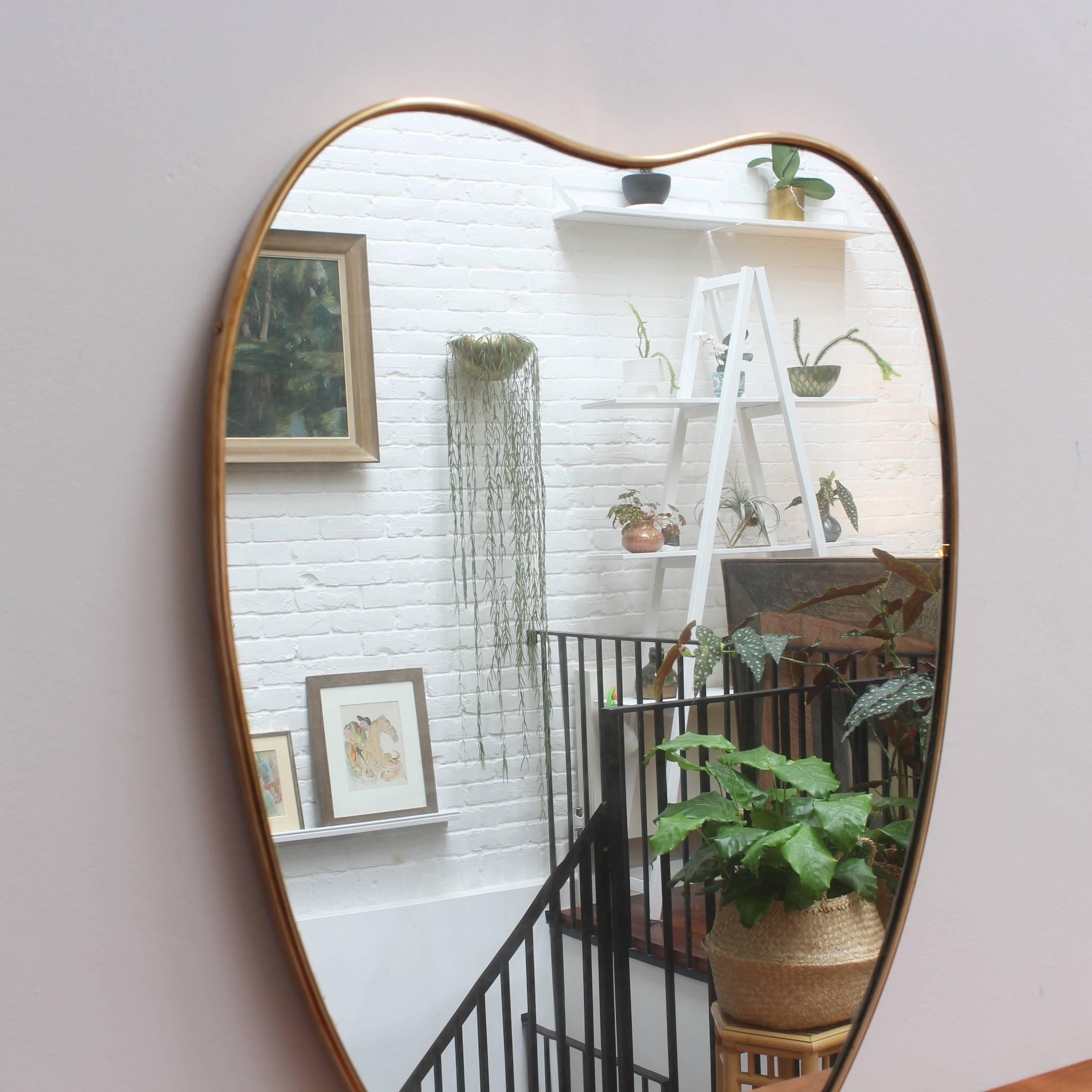 Midcentury Italian wall mirror with brass frame, circa 1950s. The mirror is apple-shaped and distinctive in a modern Gio Ponti style. This mirror is in good vintage condition. There are some evident but characterful blemishes on the brass frame and