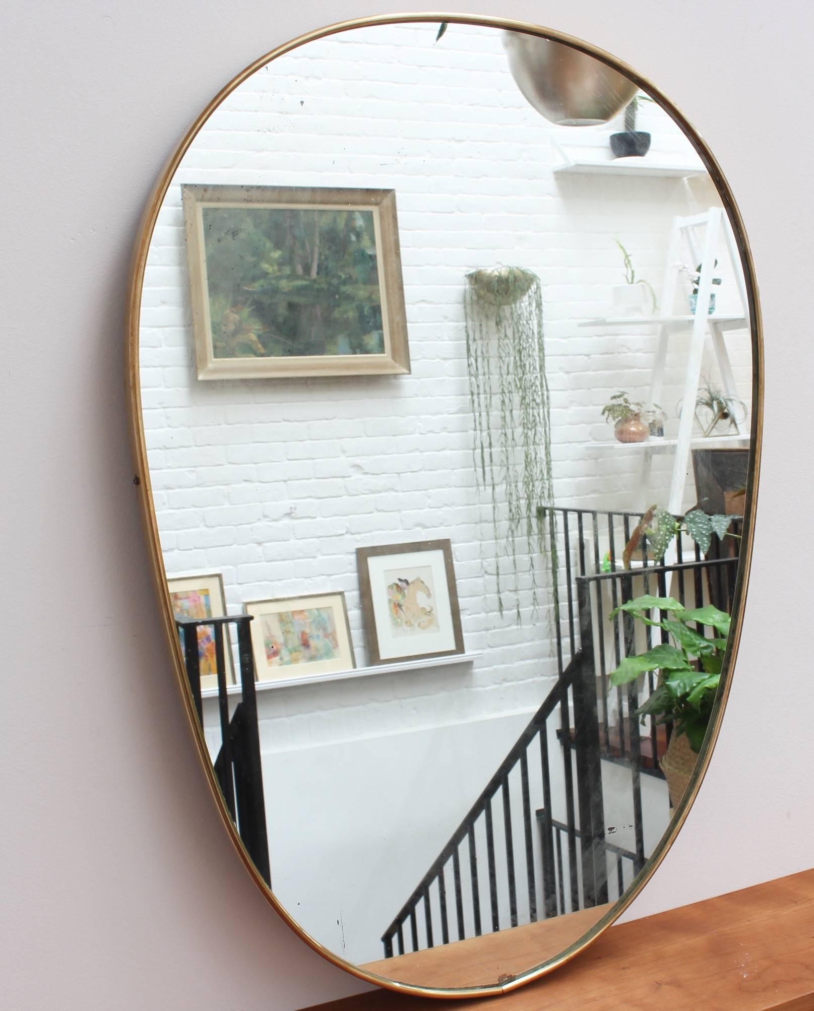 Midcentury Italian wall mirror with brass frame, circa 1950s. The mirror is unusually shaped - like an inverted egg - but always elegant and distinctive in a modern Gio Ponti style. This mirror is in good vintage condition. There are some evident