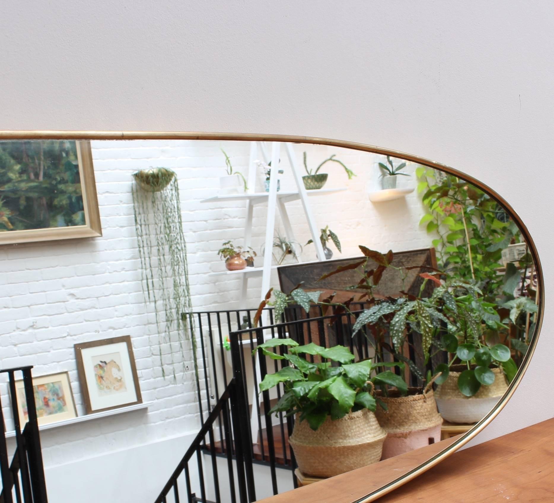 Midcentury Italian wall mirror with brass frame, (circa 1950s). The mirror is relatively large and unusually capsule shaped - very distinctive in a modern Gio Ponti style. This mirror is in very good vintage condition. There are some minor but