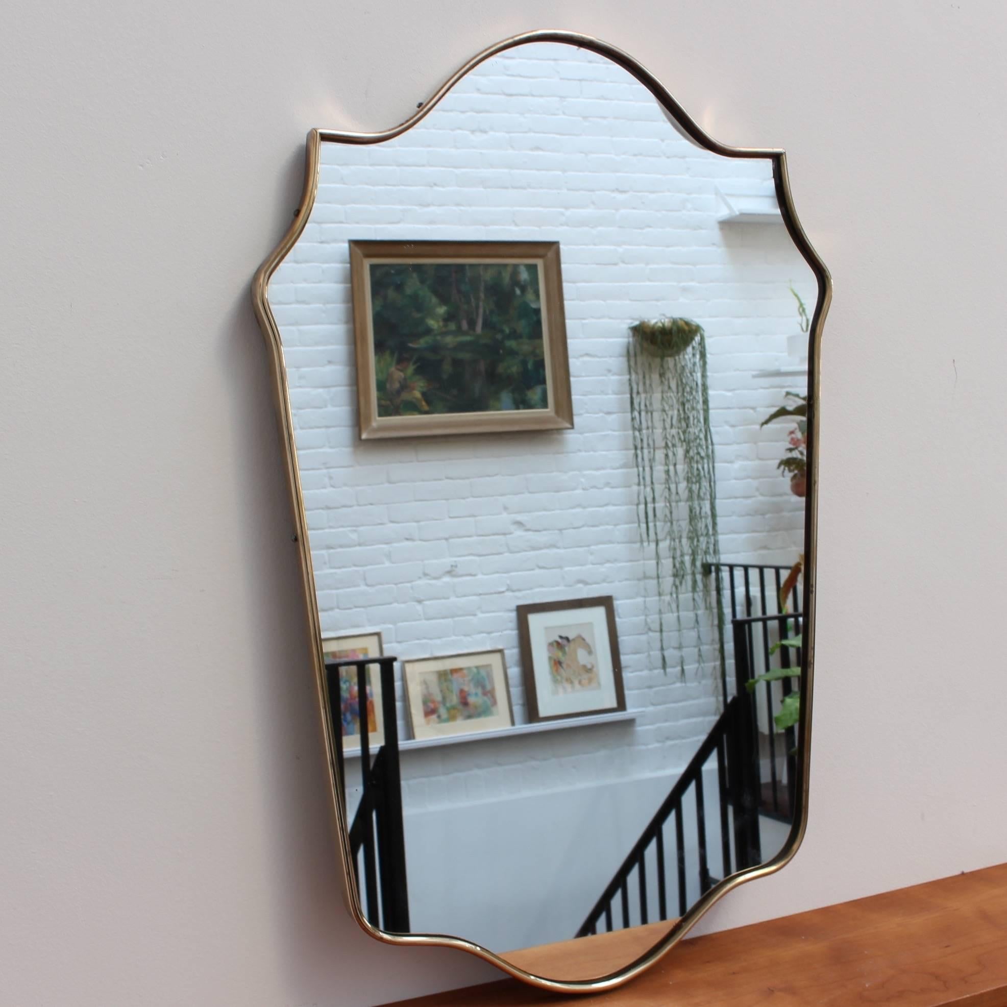 Midcentury Italian wall mirror with brass frame, circa 1950s. The mirror is crest-shaped - classically elegant and distinctive in a modern Gio Ponti style. This mirror is in good vintage condition. There are some evident but characterful blemishes