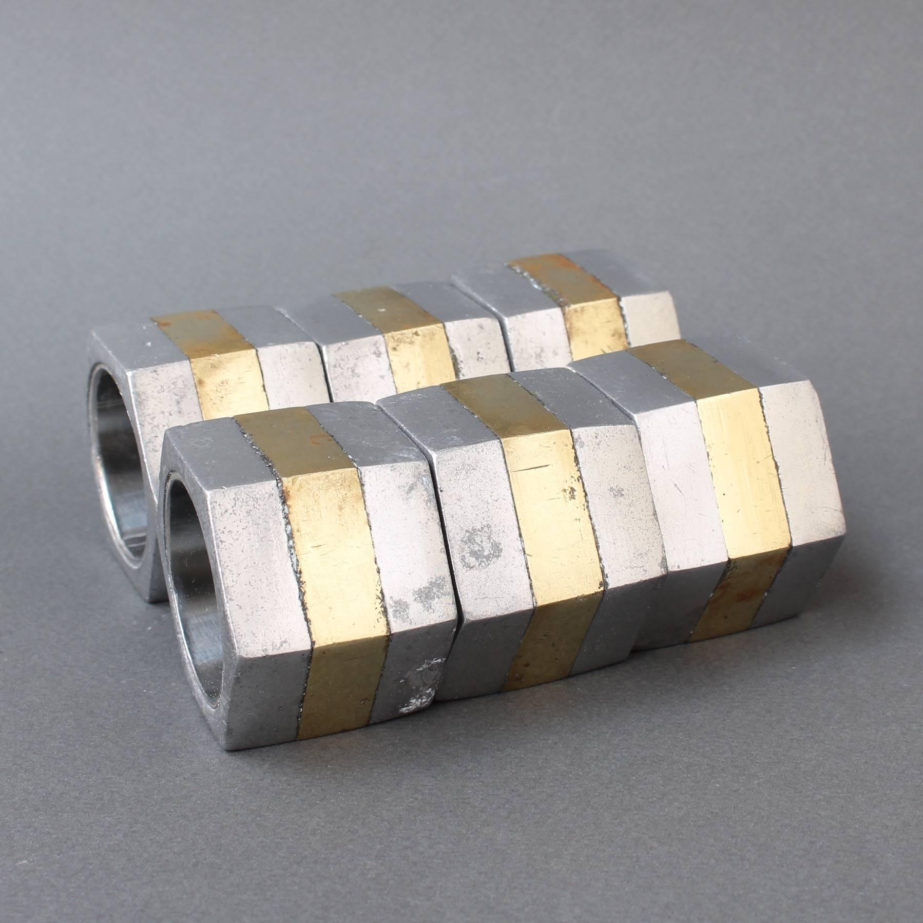 Six brutalist aluminium and brass napkin rings by David Marshall, circa 1970s. These brutalist style napkin holders are both weighty and tactile. The pieces are in good vintage condition with characterful marks and some evident blemishing consistent