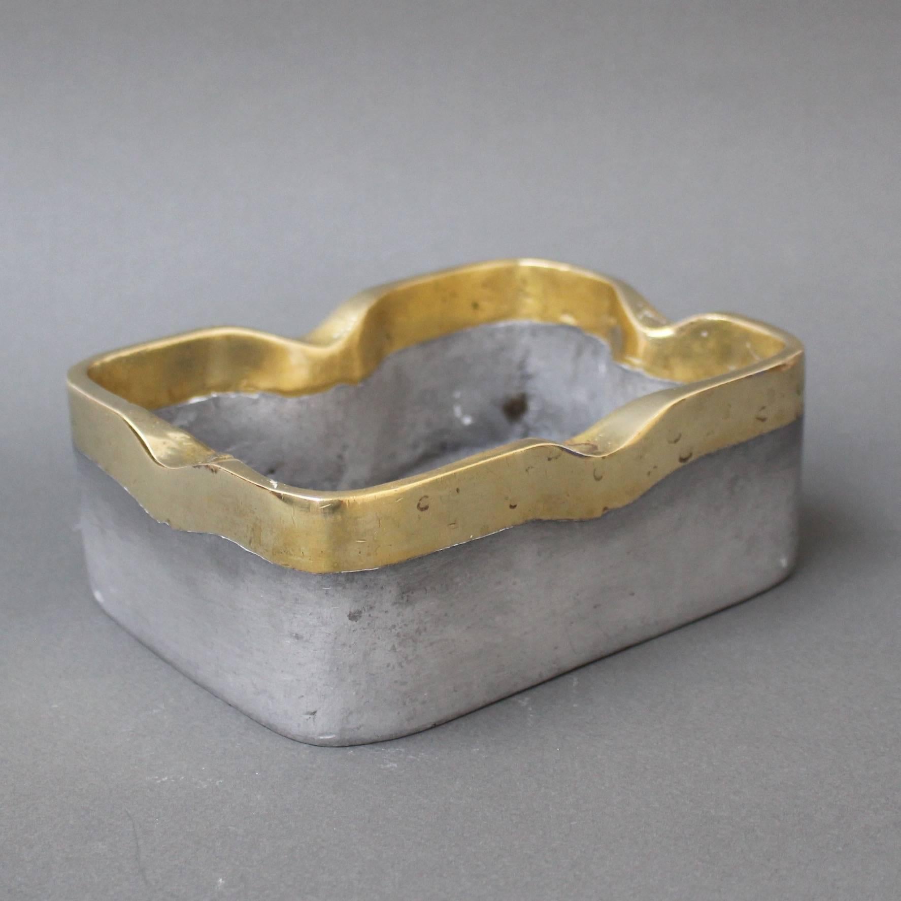 This aluminium and brass Brutalist style decorative ashtray by David Marshall is weighty and wonderfully tactile with the maker's mark impressed lightly on the aluminium side. This piece is in very good vintage condition with characterful marks