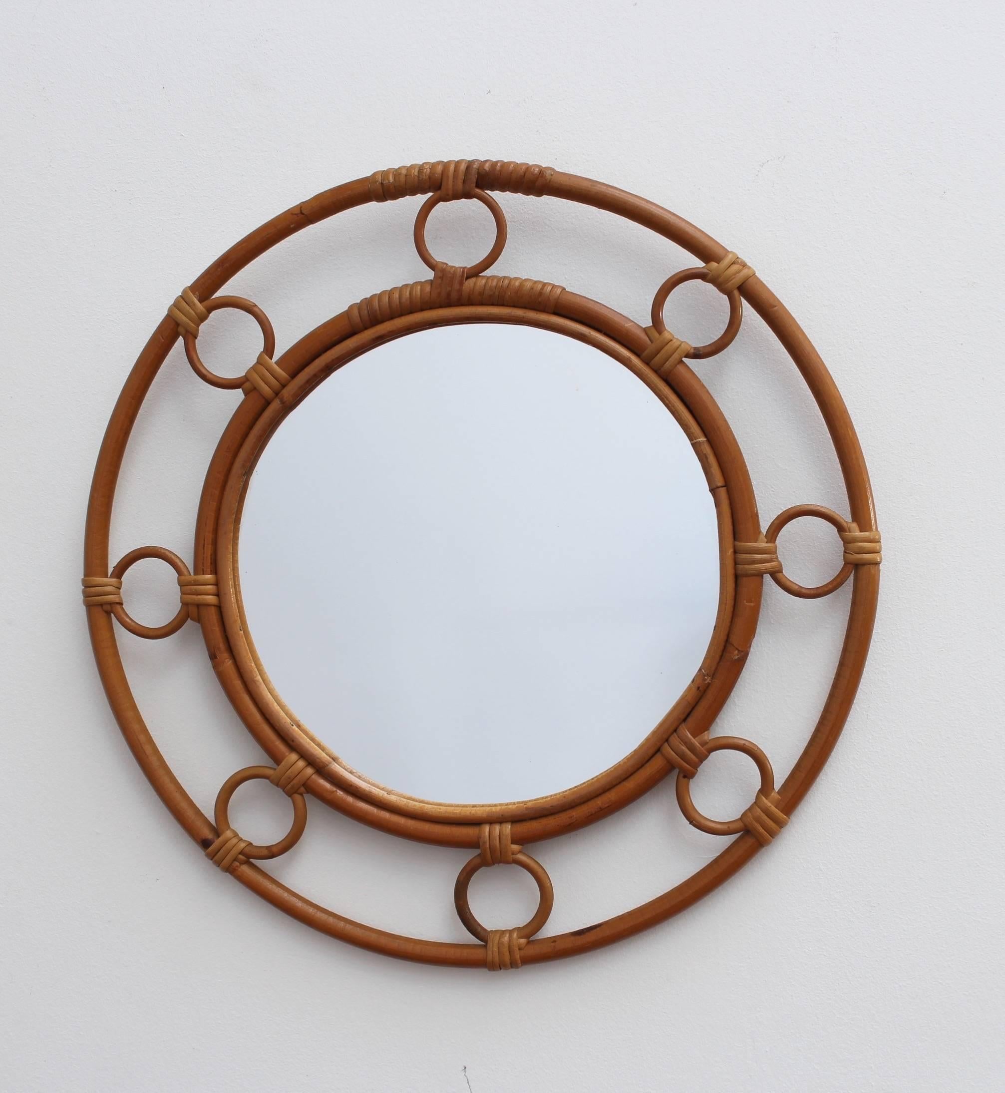 Midcentury French rattan and bamboo mirror, circa 1960s. This vintage bamboo and rattan piece is formed by two concentric circles framing the glass. They are connected by eight small rattan circles creating a chic and appealing vintage mirror. In