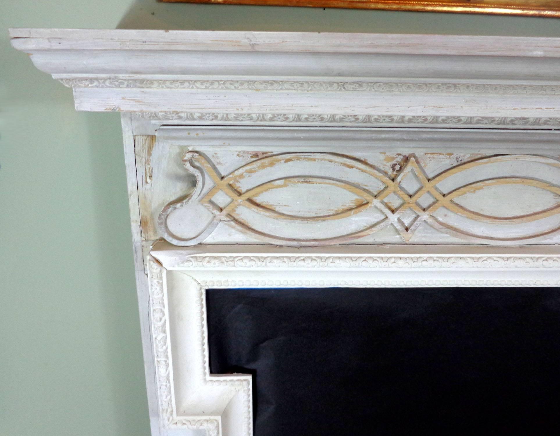 18th Century Georgian style fireplace mantel with a later painted white distressed finish. The opening is surrounded with a carved plaster molding that was added later.
 
