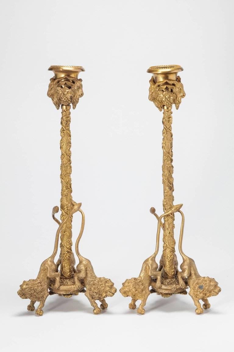 A pair of whimsical gilt bronze candlesticks with cast rams and lions. The lions have long curving tails to support the candlestick on paw and ball feet.
