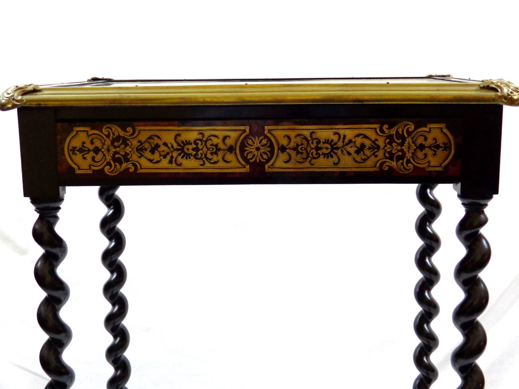Ebonized side table with a single drawer, barley twist legs, panels with gilt decoration, and a glass top framed with bronze doré, in the style of André-Charles Boulle (1642-1732).