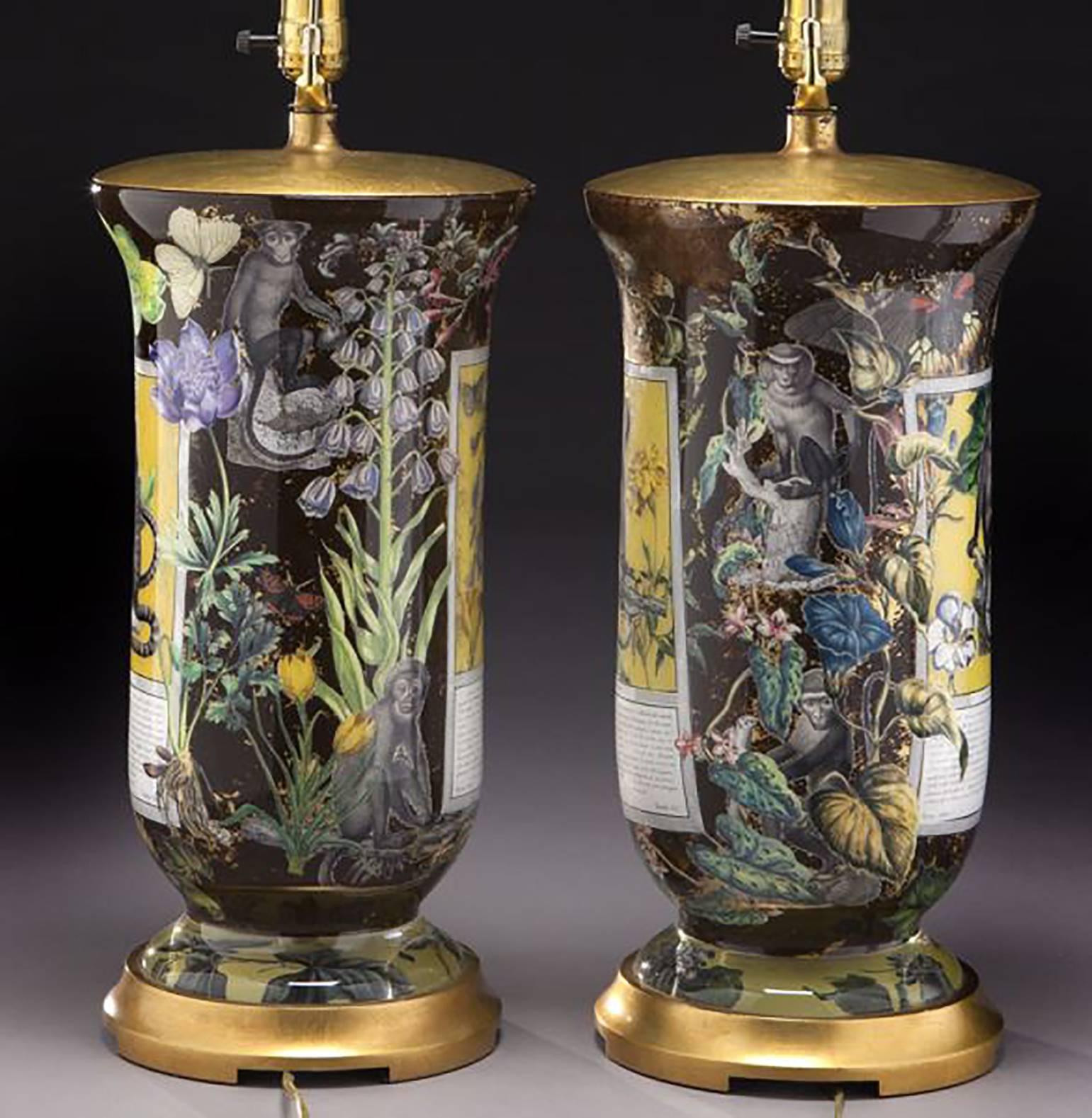 Pair of glass table lamps beautifully reverse decorated by hand with scenes of marmosets, flowers and butterflies on gilt metal plinths, with pleated shades.
