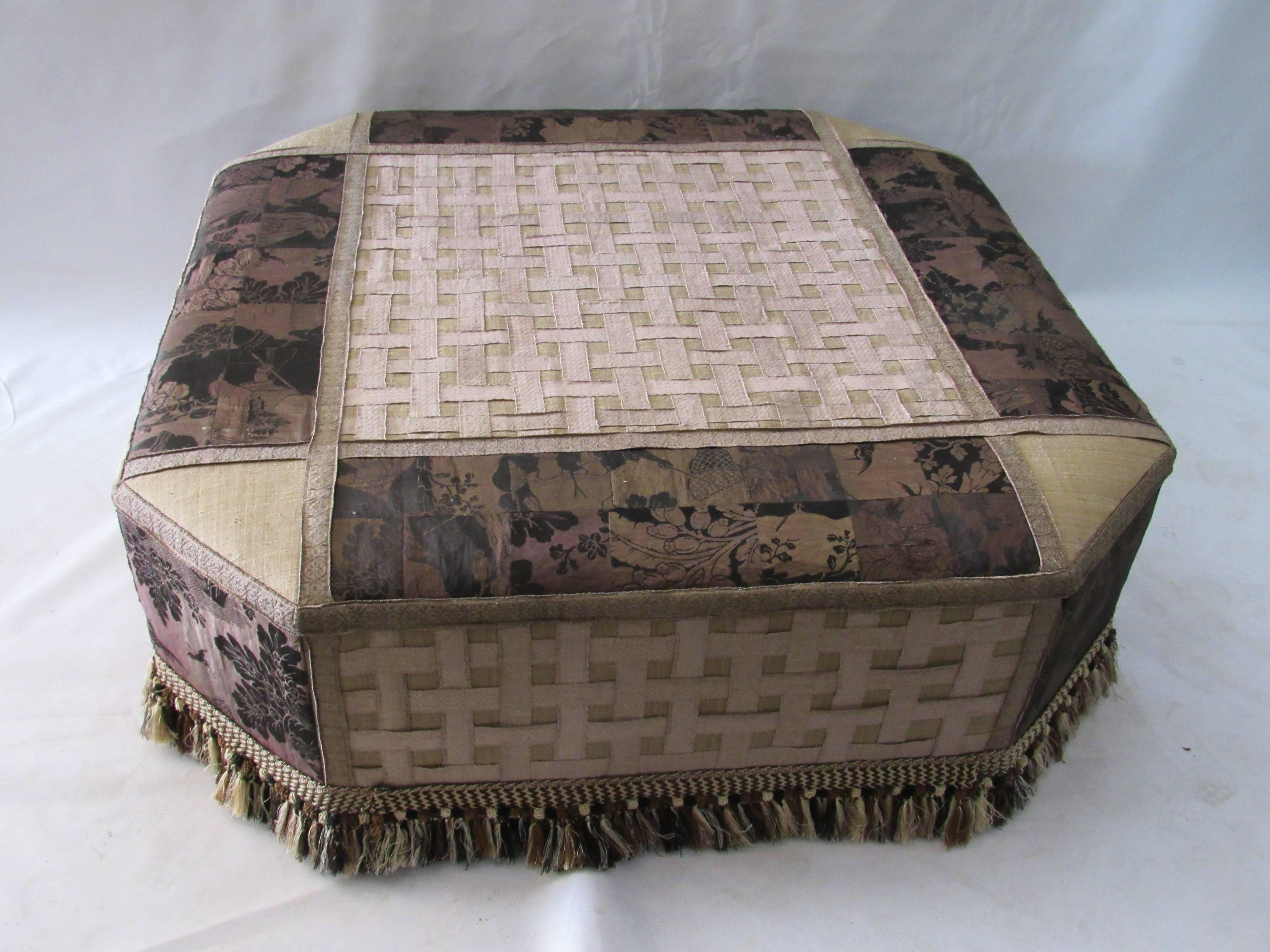 Sophisticated ottoman with antique upholstery. The square shaped ottoman with canted corners is upholstered with beautiful woven black and brown damask with gold thread. It has been sewn in a patch work design and is applied with borders of old