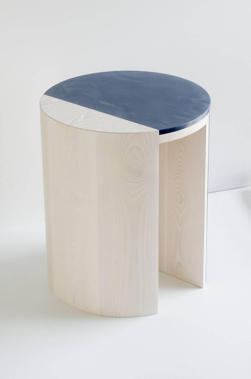 The Gibbous side table pairs wood and solid surface to create a complex and striking Silhouette. The table uses essential elements like the circle, volume, and line in surprising ways, creating a sense of movement through the piece. Lacquered