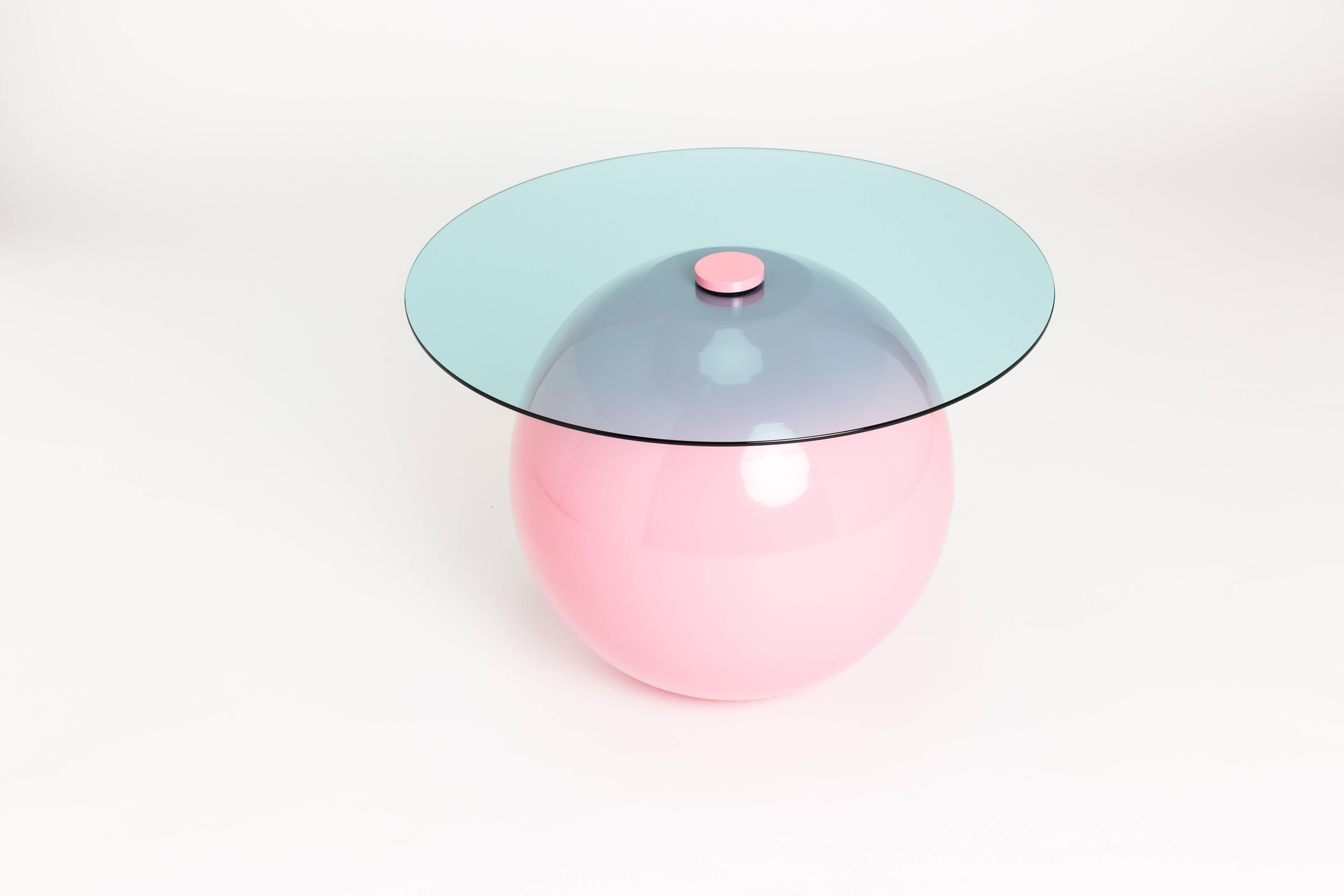 A coffee table suitable for both indoor and outdoor use. The base is constructed from two hand spun hemispheres perfectly married together. The top is secured via an oversized bolt. The base is pictured in a pink powder coat with blue tint glass