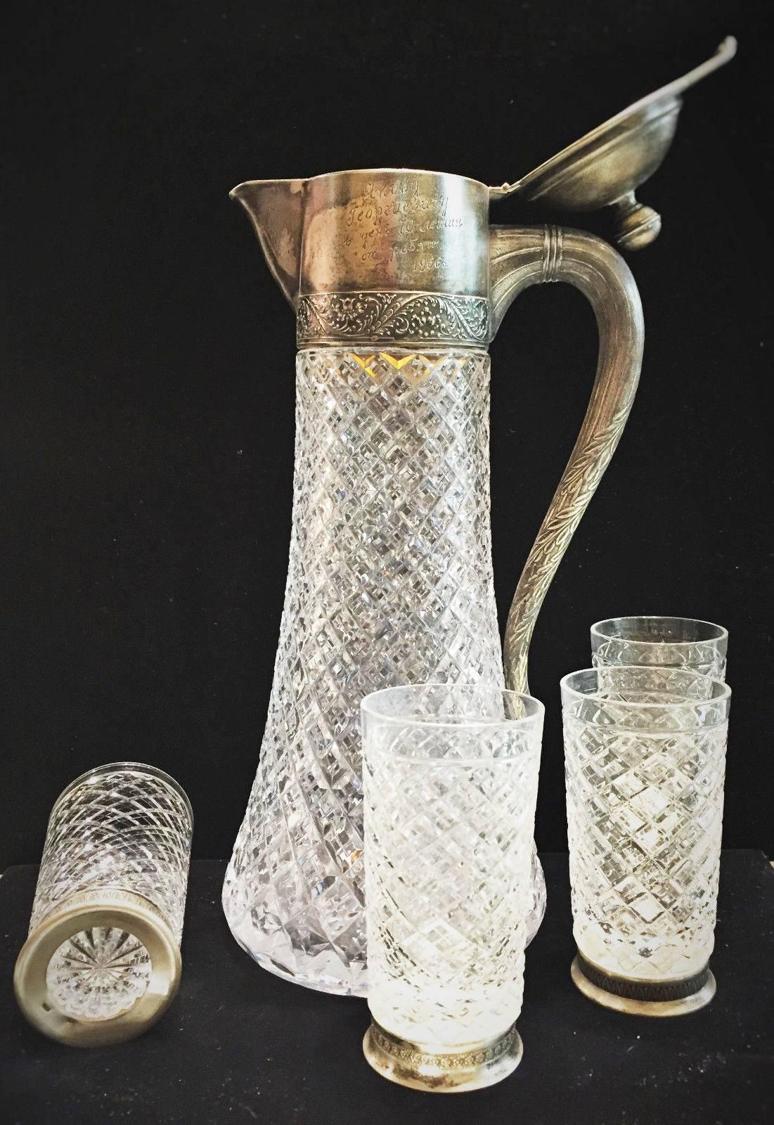 This elegant vintage Soviet Russian cut crystal and silver set of wine pitcher and twelve glasses consists of a tall pitcher with the gold-plated inner part of the neck and cover and twelve matching glasses with the silver rim featuring repeating