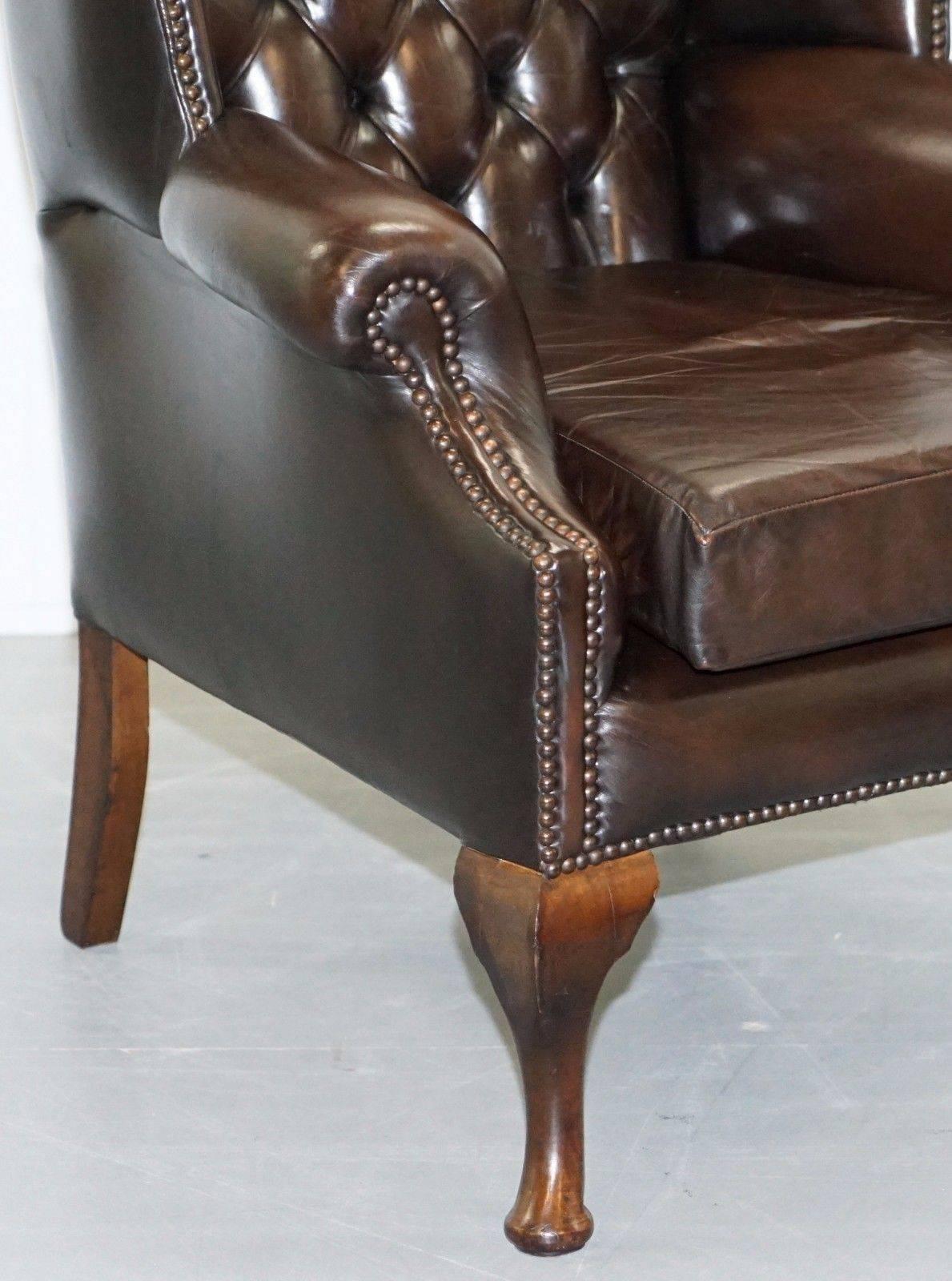 Hand-Carved Pair of 1960s Aged Brown Leather Chesterfield Wingback Armchairs and Footstool