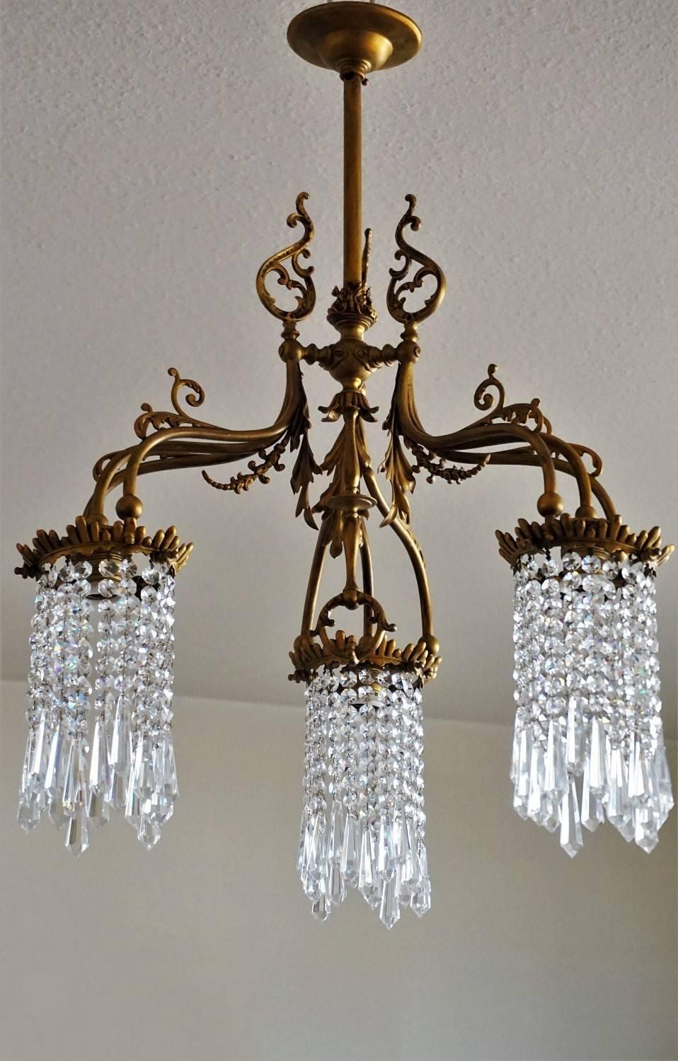 Art Nouveau Style bronze and brass chandelier, three lamp arms with crystal hangings surrounding the light bulbs, circa 1920.

Measures: Height 30 in (76 cm)
Width/Depth 21 in (53 cm)
Thee large light sockets.