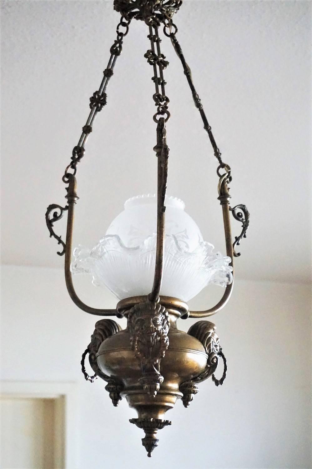 This empire style oil light has been electrifed at a later time. Brass body ornate with lion heads, three chains connecting to a decorative ceiling canopy. Beautiful two-piece etched glass shade, single large bulb socket under the glass