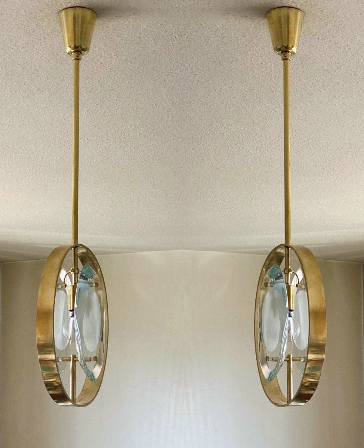 A pair of  iconic design pendants by Max Ingrand for Fontana Arte, Model 1933, Italy, 1961. Organically shaped double lens cut panels of thick profiled polished Murano glass with sandblasted centers fitted within a natural brass ring suspended from